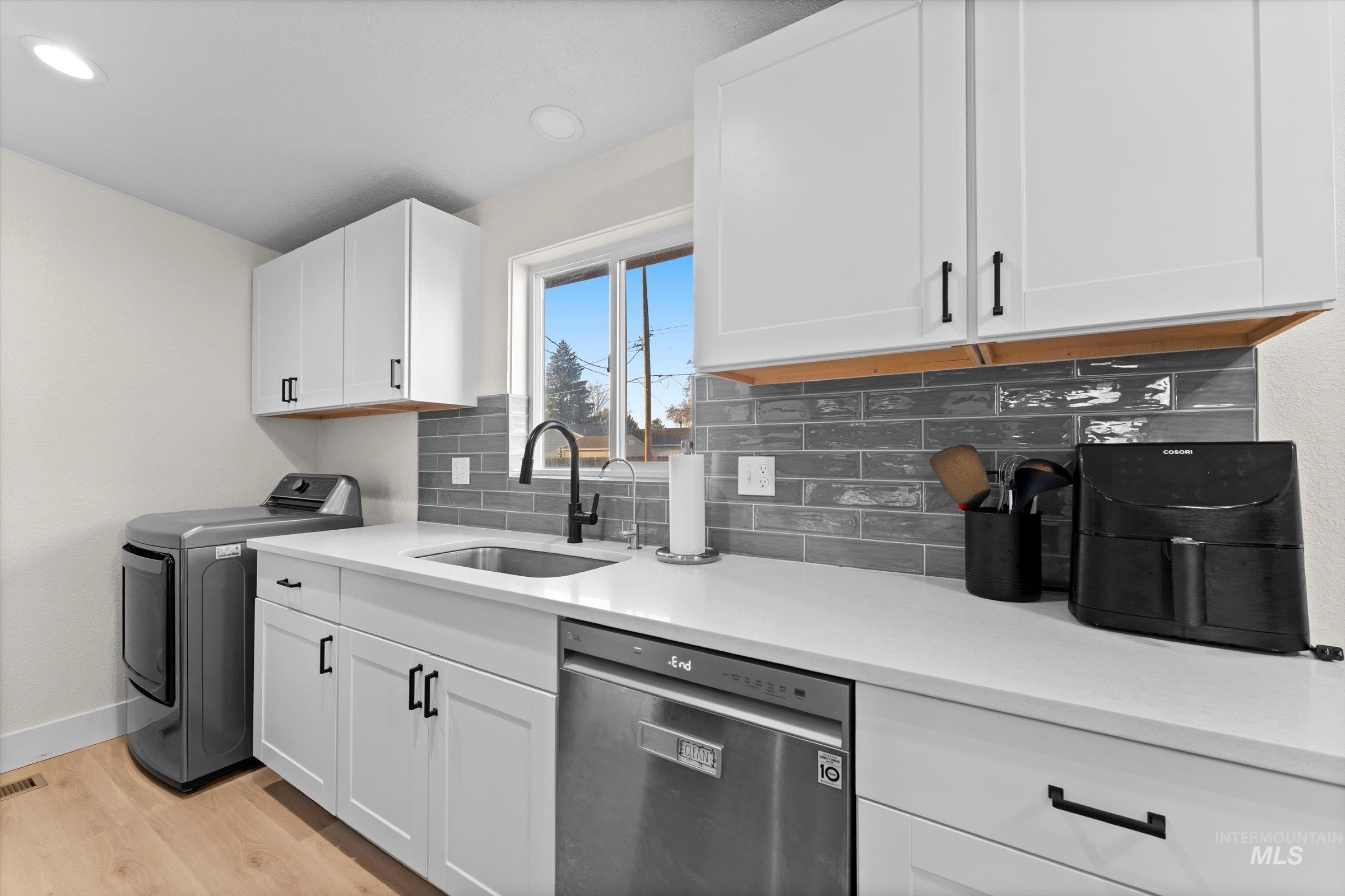 Kitchen featuring washer / dryer, dishwasher, white cabinets, light wood-style floors, and backsplash