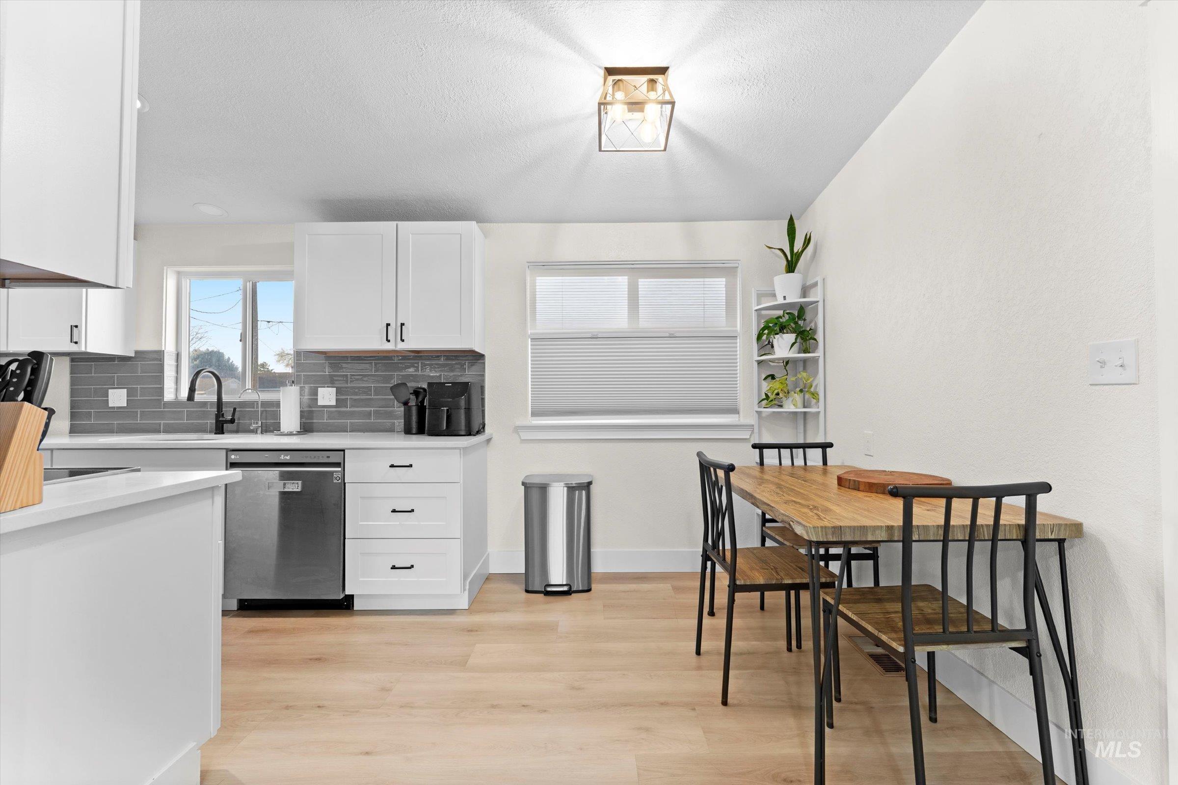 Kitchen with decorative backsplash, white cabinetry, stainless steel dishwasher, light wood-style floors, and light stone counters