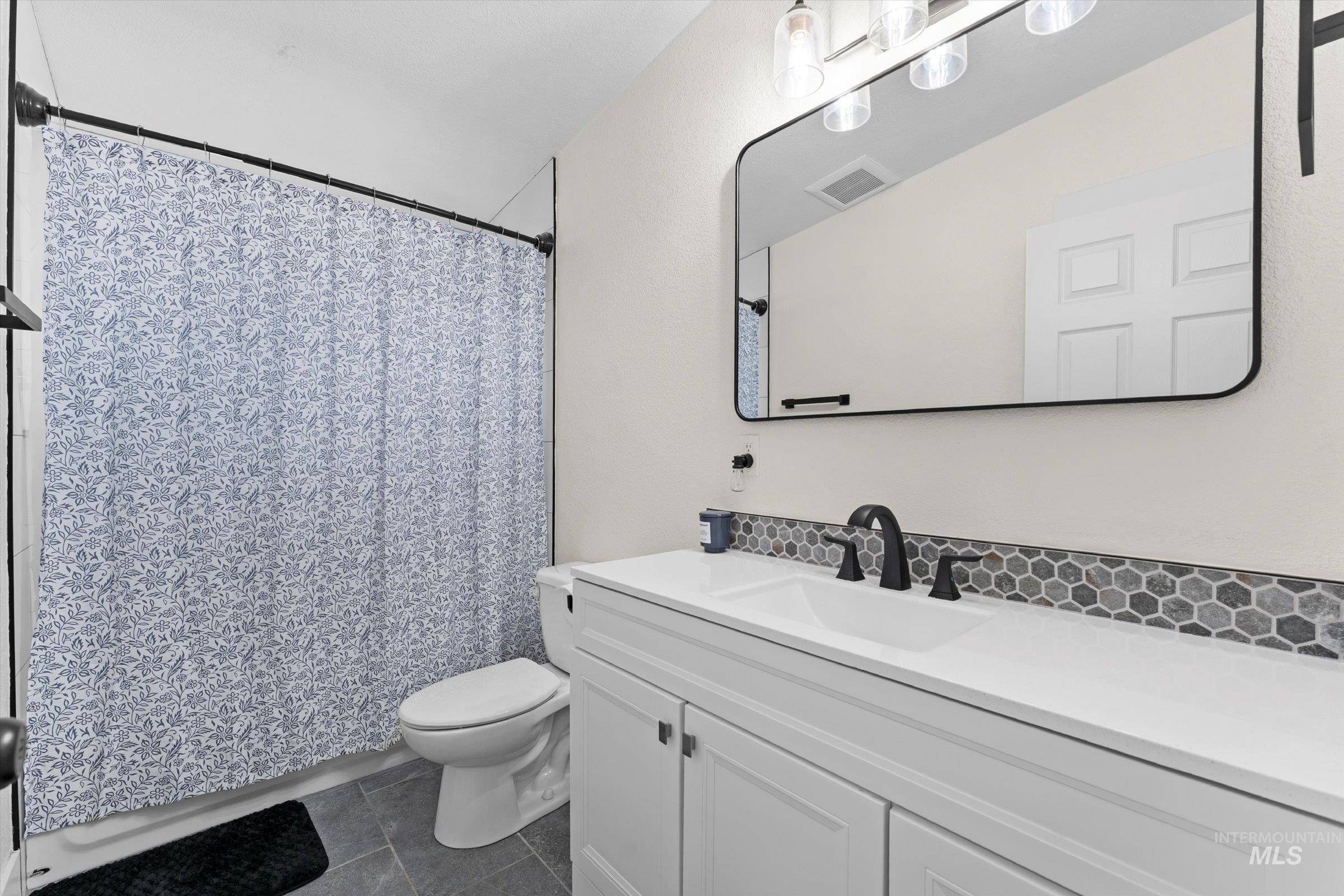 Full bathroom featuring vanity, curtained shower, and dark tile patterned flooring