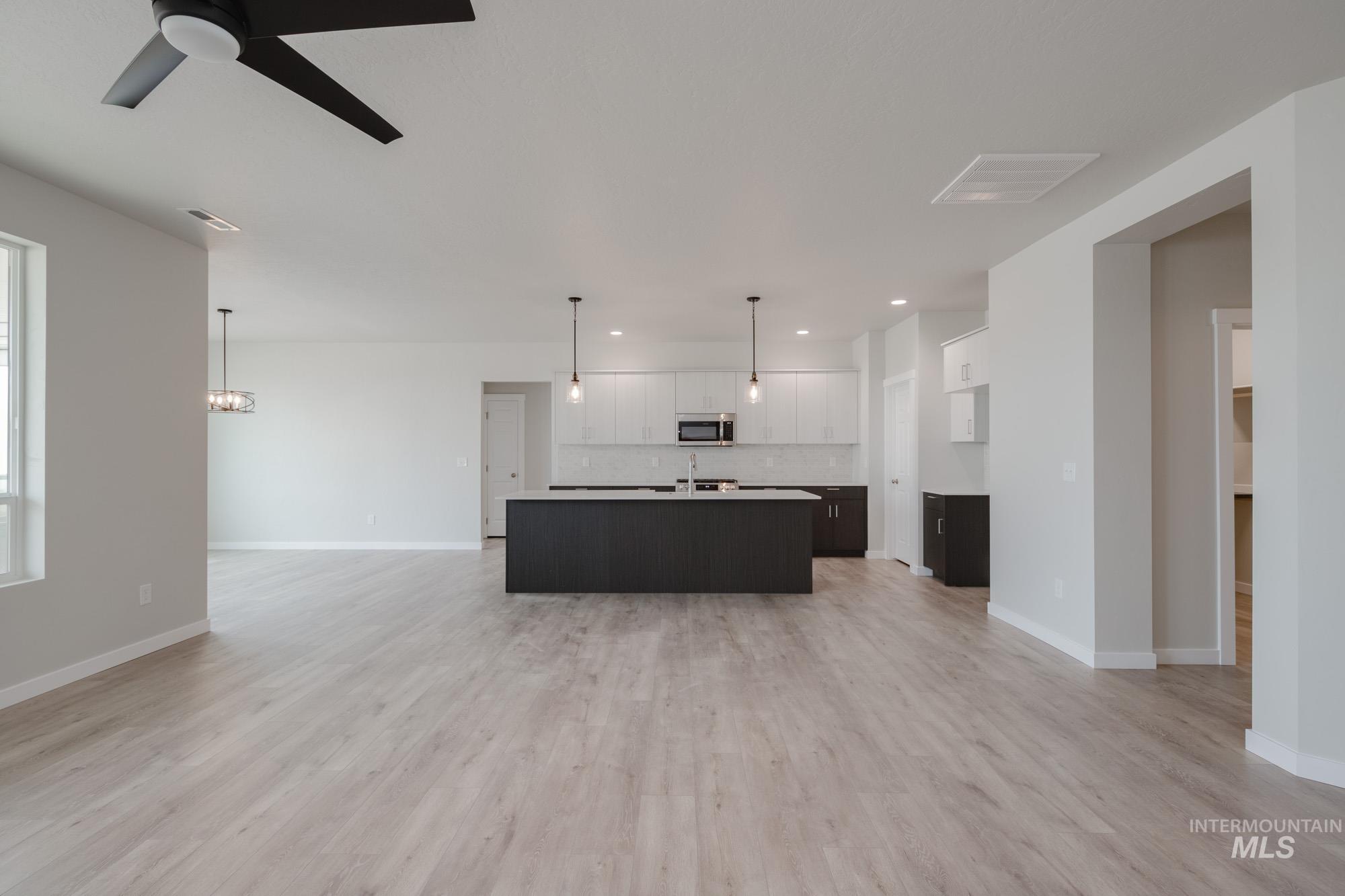 Kitchen with open floor plan, a center island with sink, hanging light fixtures, white cabinetry, and light countertops