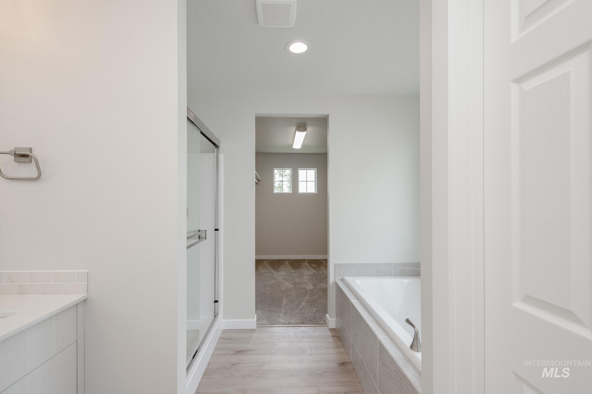 Bathroom featuring a garden tub, vanity, a stall shower, light wood-style floors, and recessed lighting