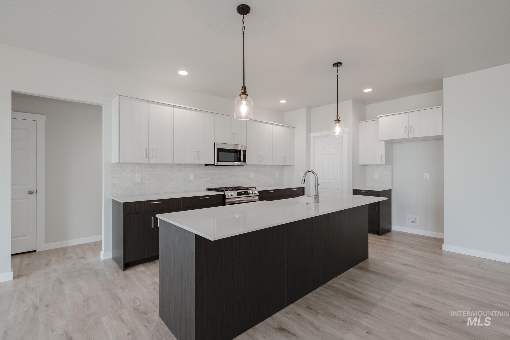 Kitchen with white cabinets, tasteful backsplash, decorative light fixtures, stainless steel appliances, and an island with sink
