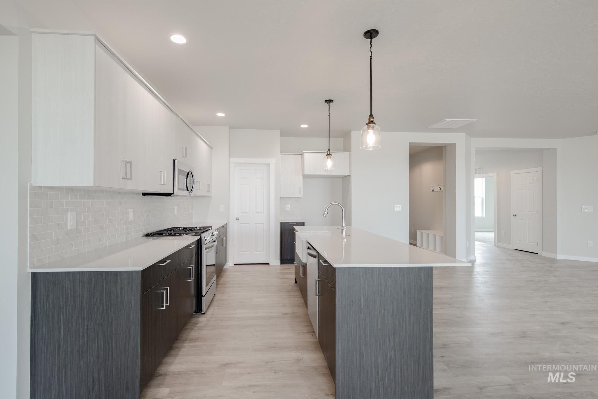 Kitchen featuring stainless steel appliances, white cabinets, pendant lighting, a center island with sink, and tasteful backsplash