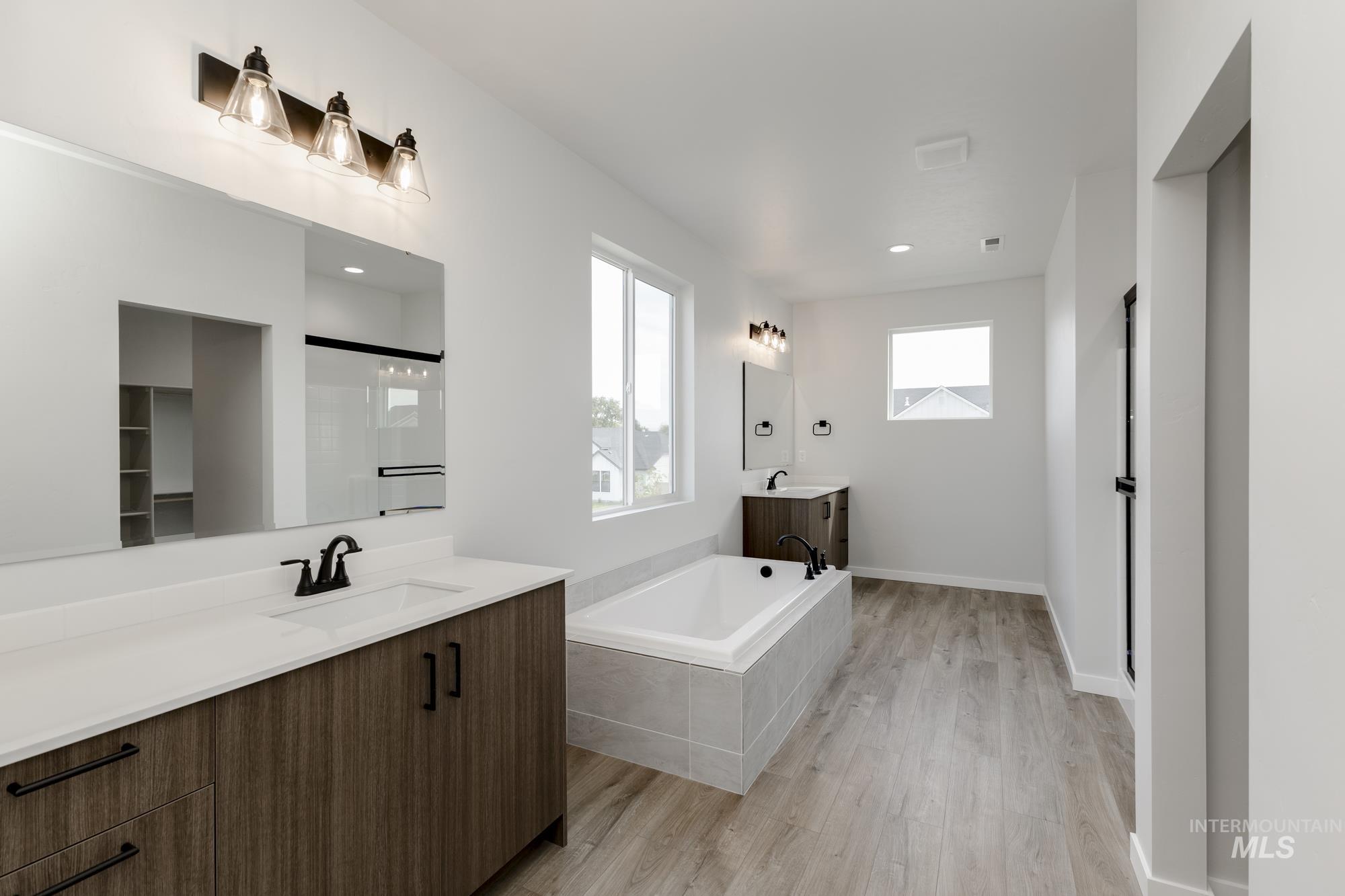 Bathroom featuring two vanities, a stall shower, a garden tub, and light wood-style flooring