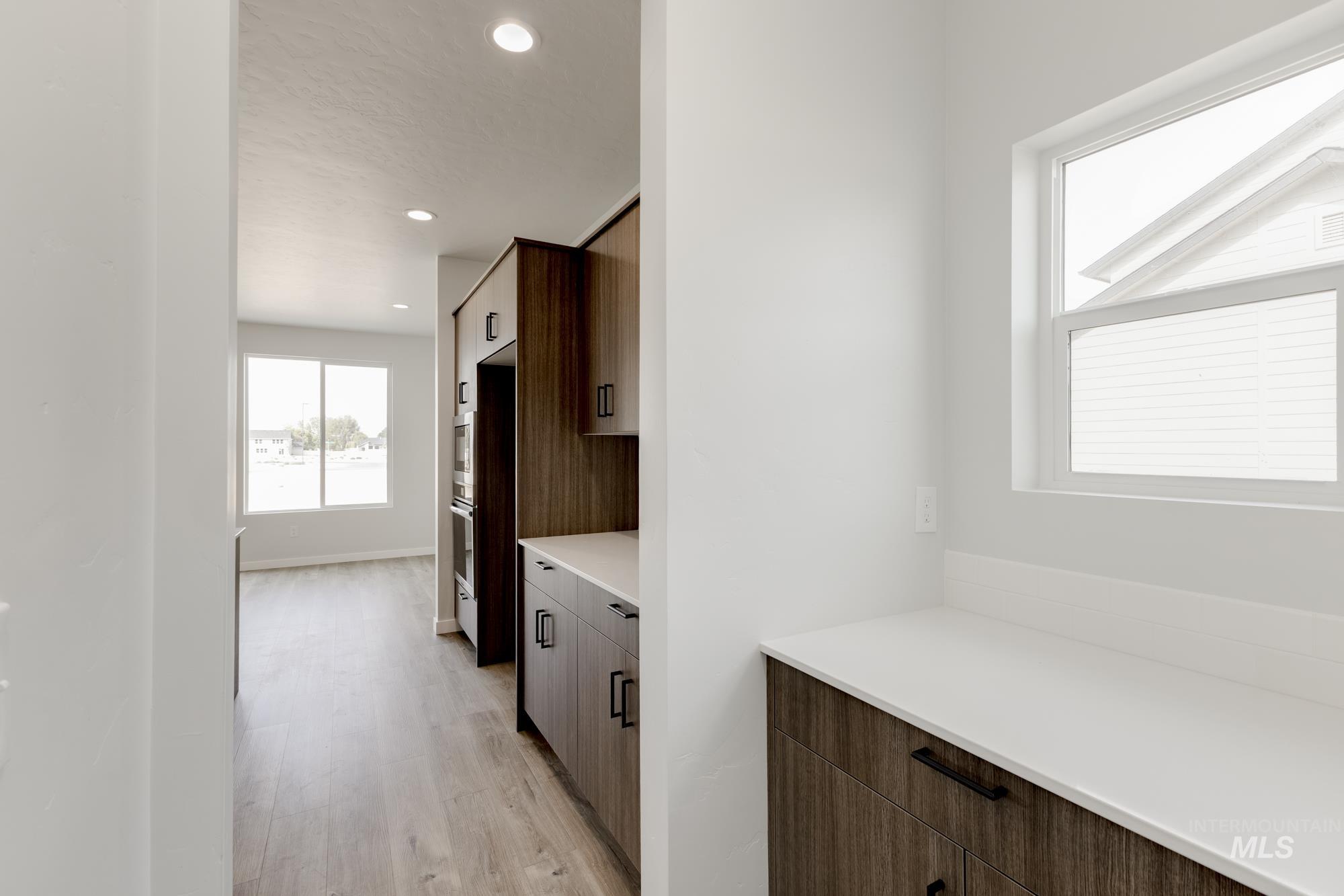Kitchen featuring modern cabinets, light wood finished floors, recessed lighting, brown cabinetry, and light stone counters