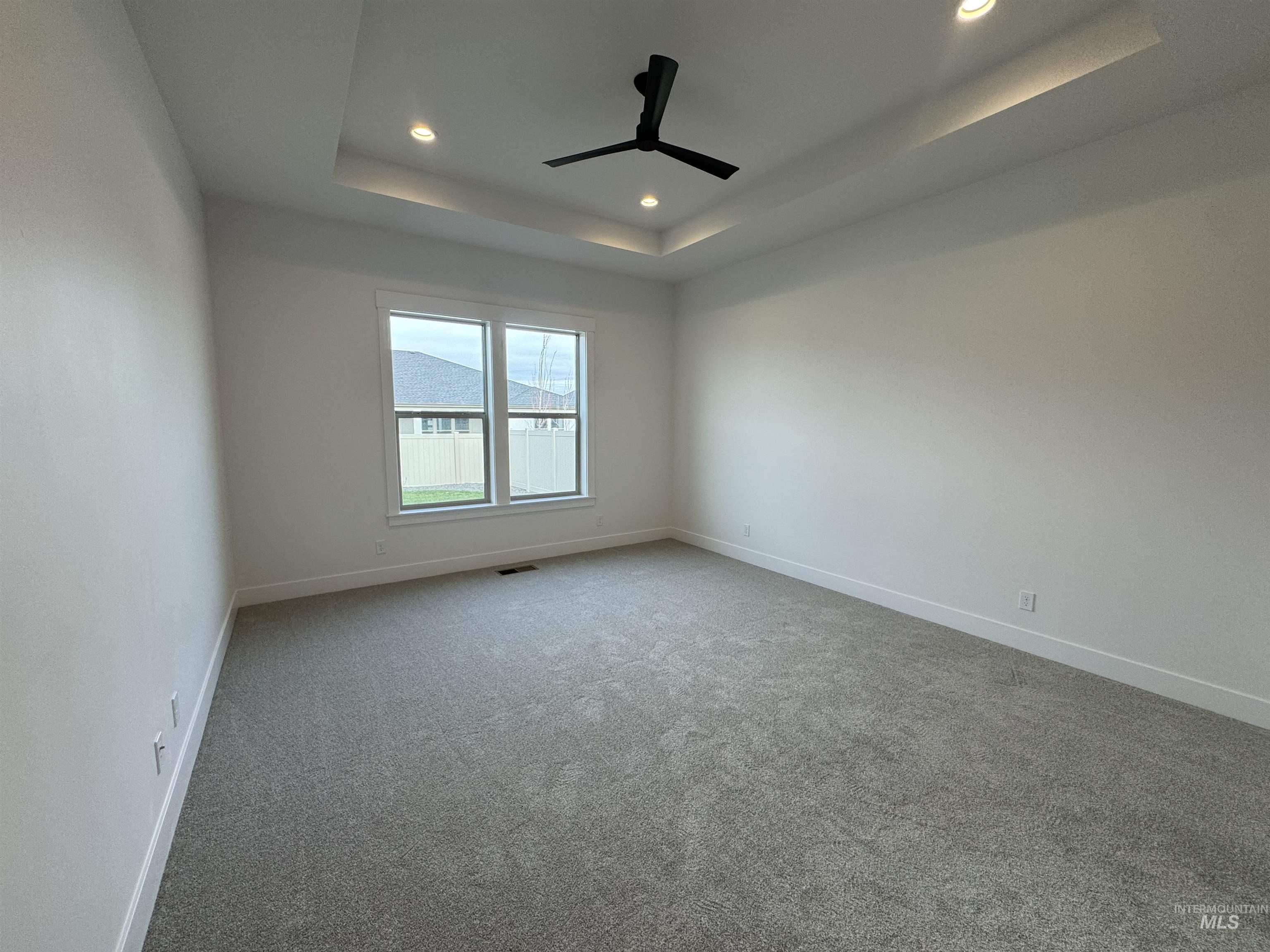 Empty room with a tray ceiling, carpet, recessed lighting, and ceiling fan