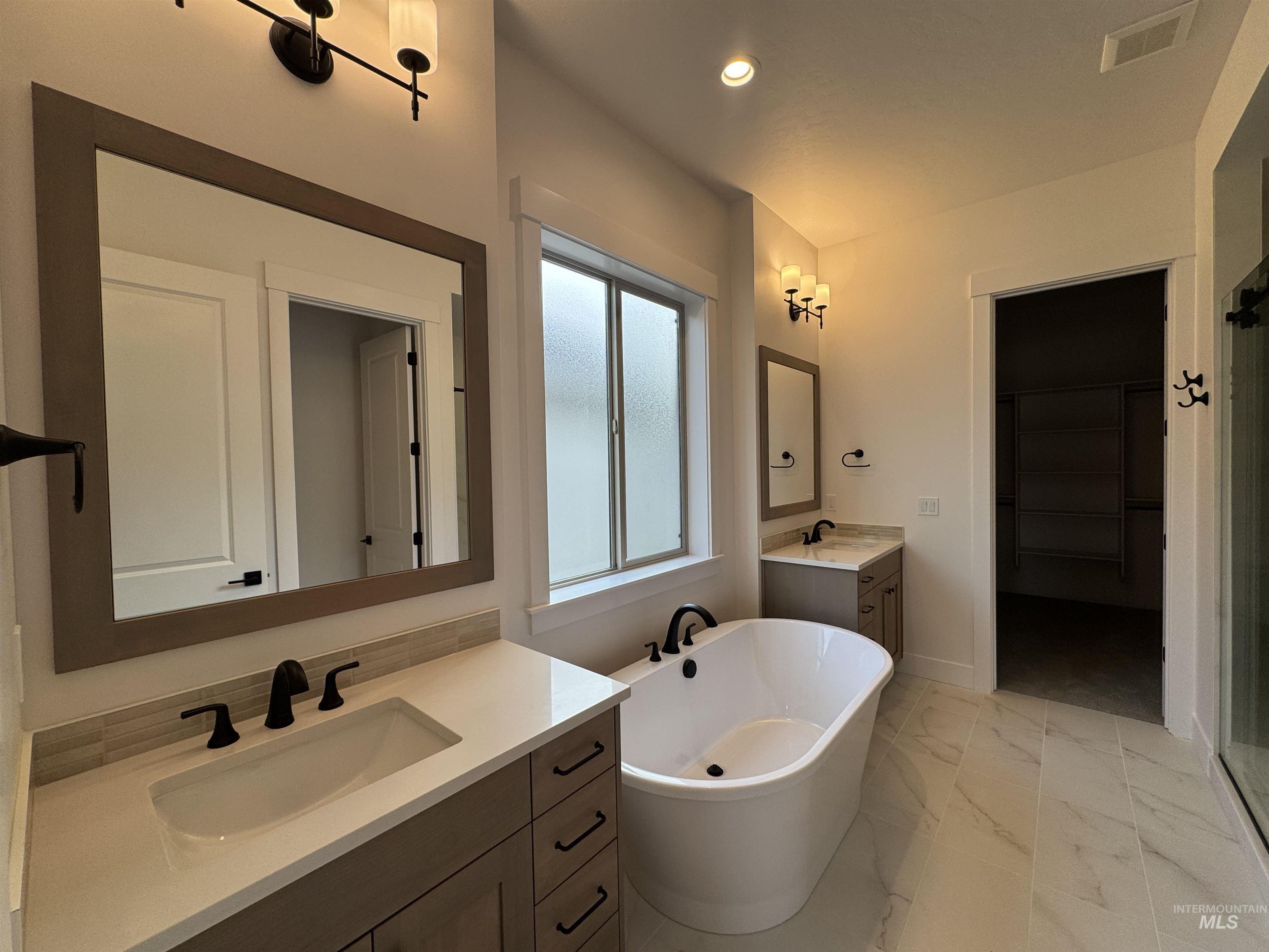 Bathroom with two vanities, light marble finish flooring, a walk in closet, a freestanding bath, and a shower stall