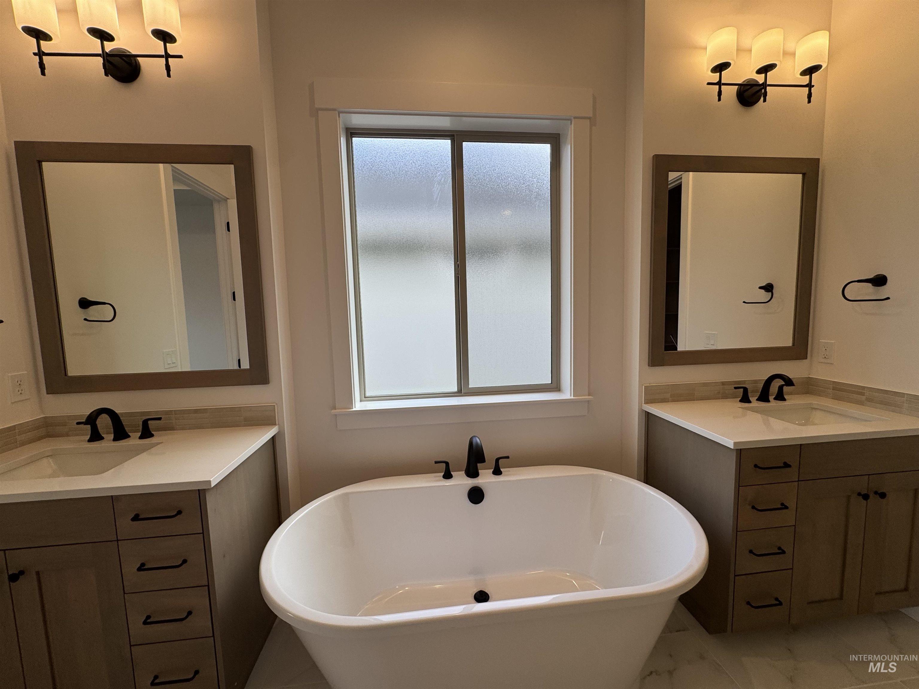 Full bath featuring a freestanding bath, light marble finish floors, and two vanities