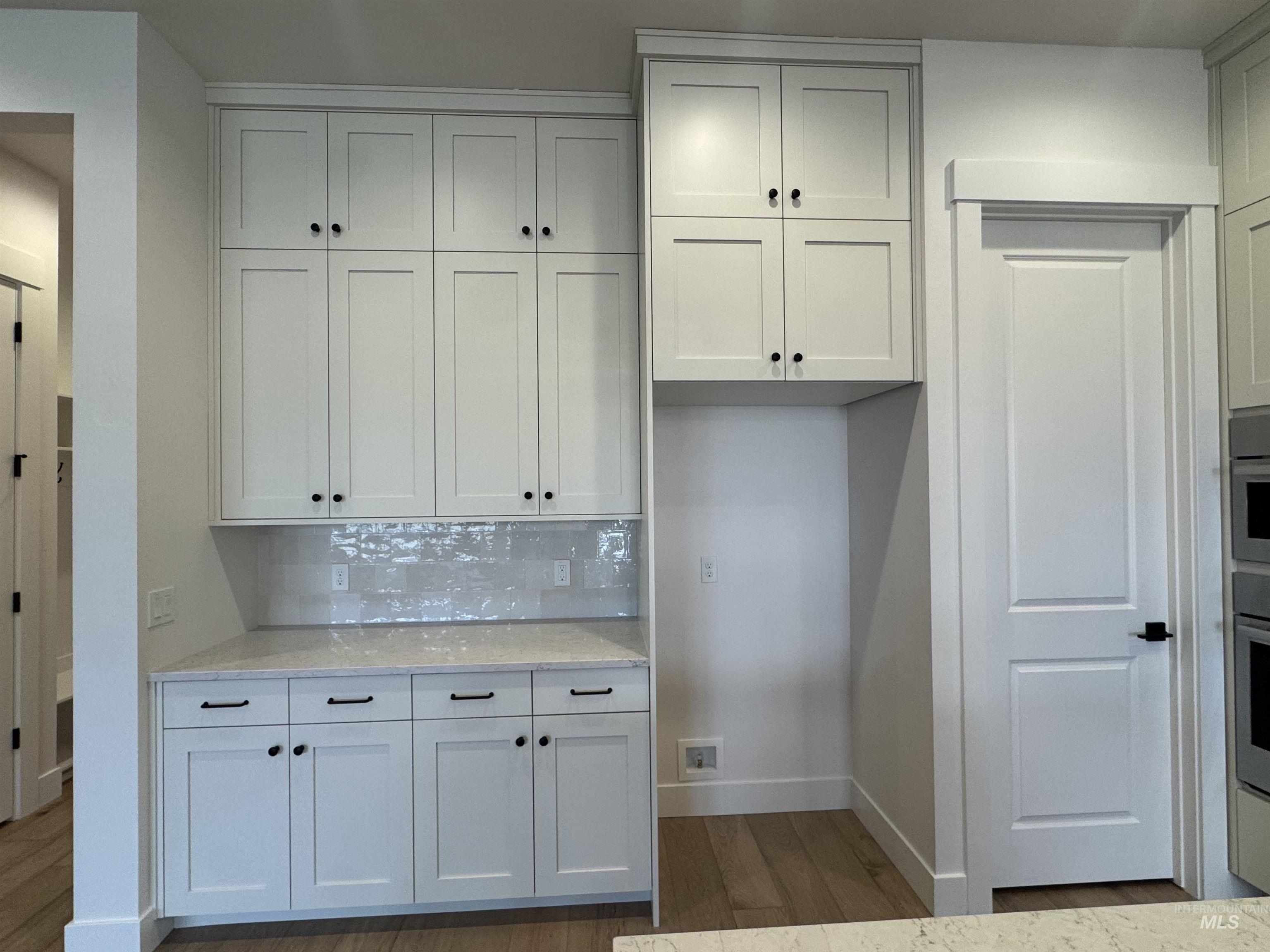 Kitchen featuring white cabinets, light stone countertops, light wood-type flooring, and backsplash
