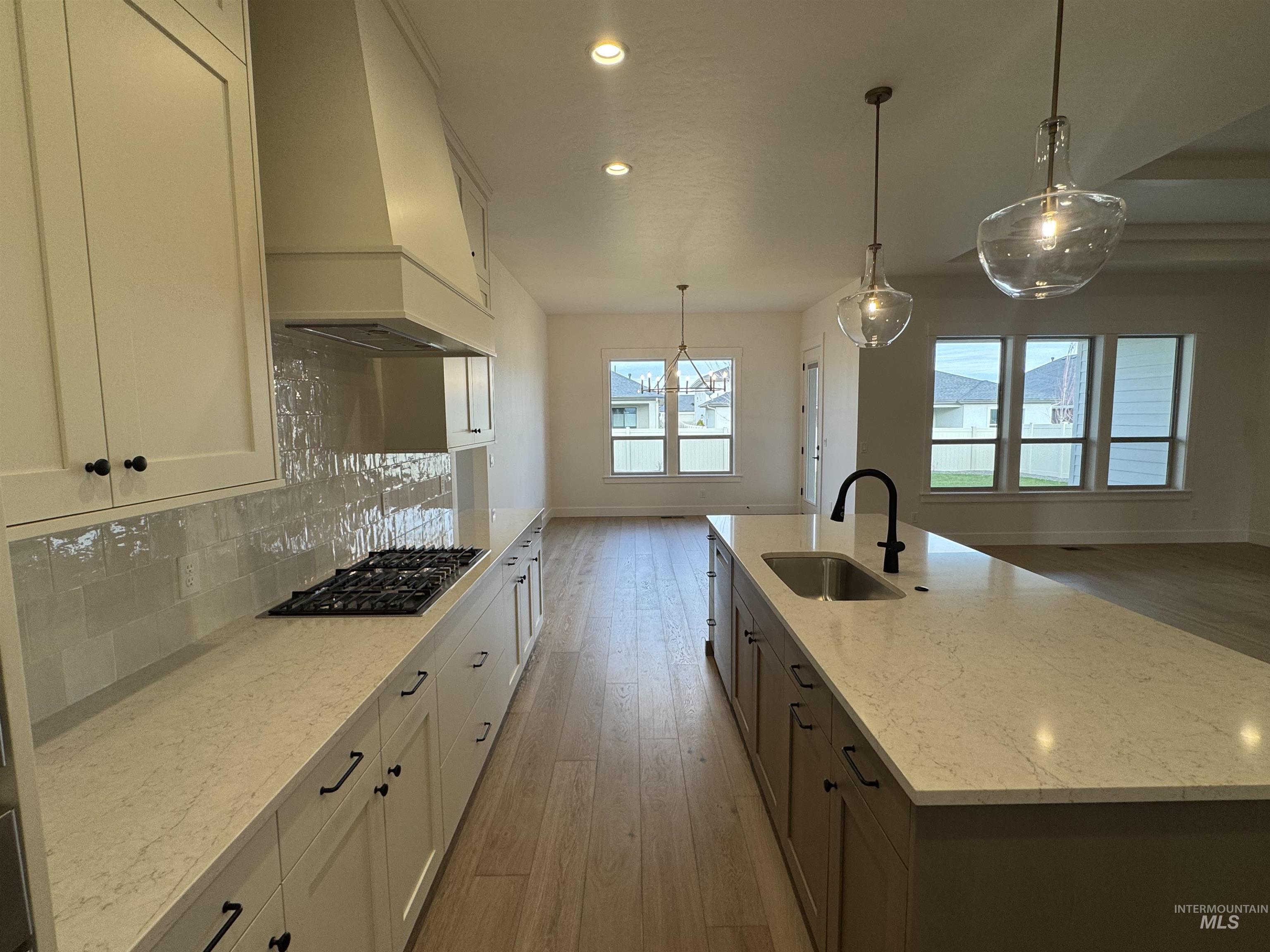 Kitchen featuring white cabinets, decorative light fixtures, light wood finished floors, an island with sink, and recessed lighting