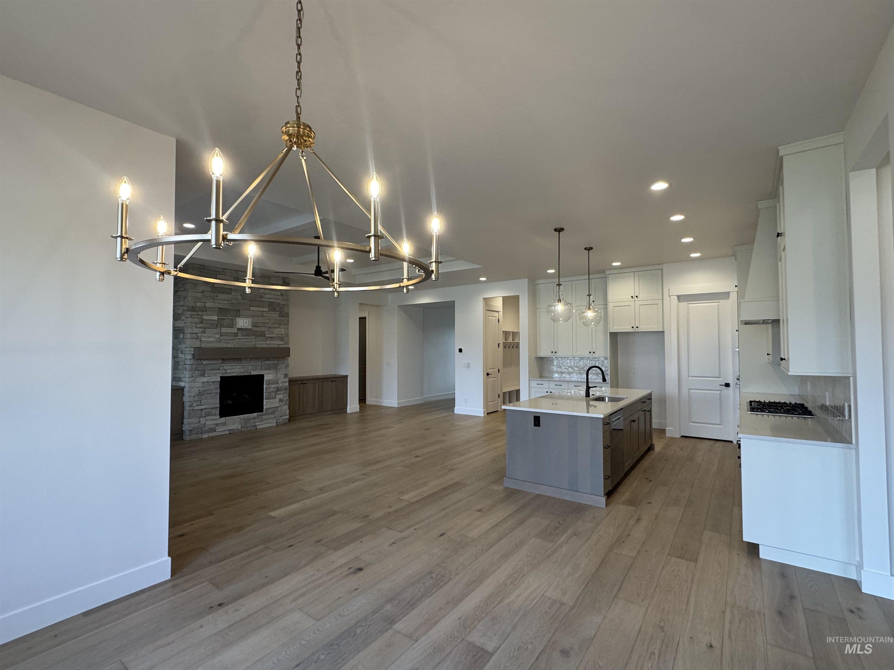 Kitchen featuring open floor plan, a chandelier, white cabinetry, a kitchen island with sink, and a stone fireplace