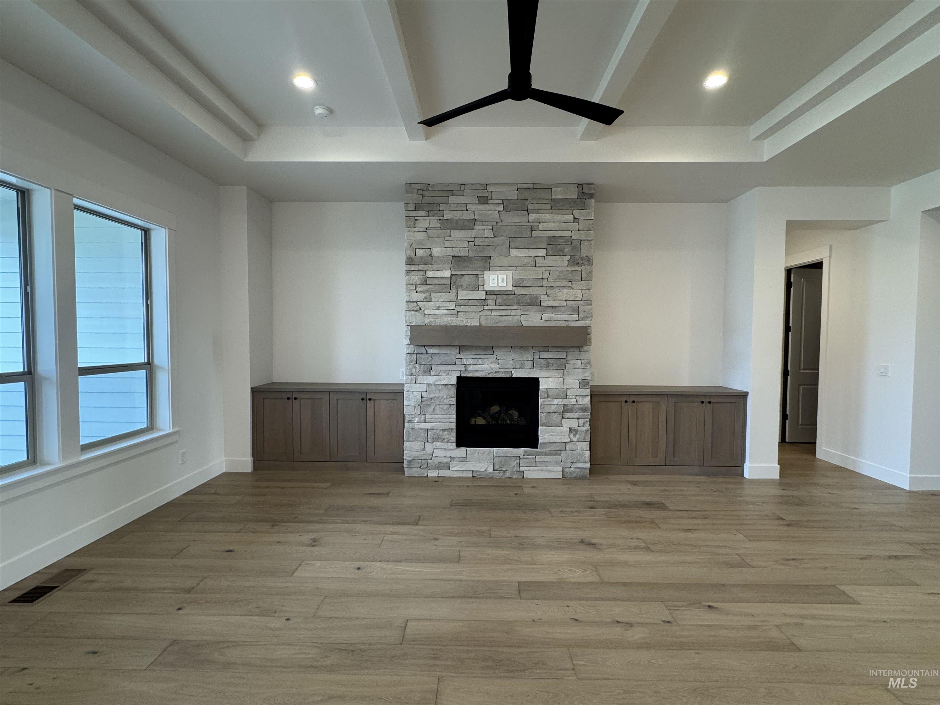 Unfurnished living room featuring a fireplace, wood finished floors, ceiling fan, a raised ceiling, and beamed ceiling