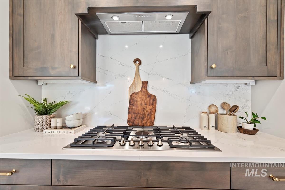 Kitchen featuring exhaust hood, stainless steel gas cooktop, and light stone counters