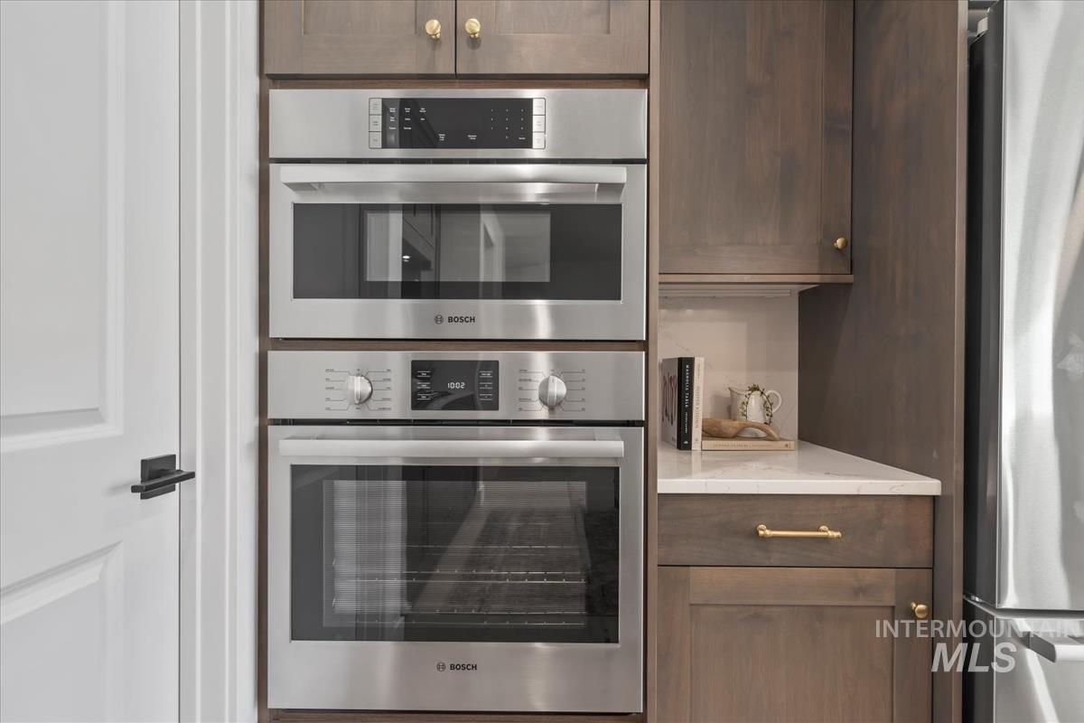 Kitchen with appliances with stainless steel finishes, dark brown cabinets, and light stone counters