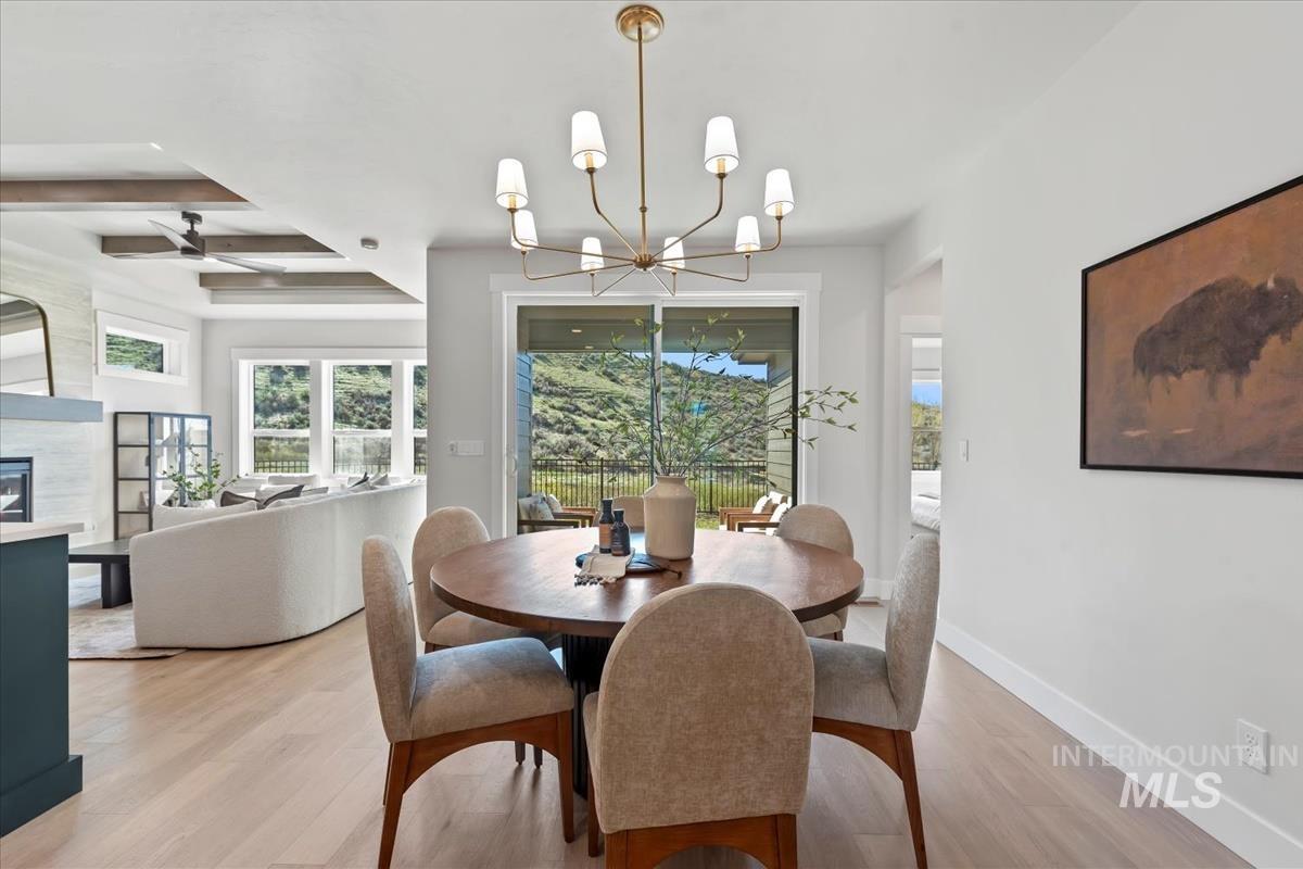 Dining space with light wood finished floors, a chandelier, healthy amount of natural light, beamed ceiling, and a glass covered fireplace