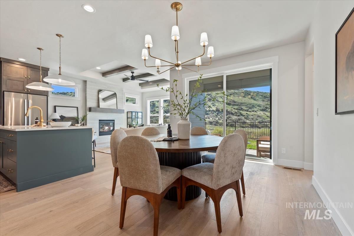 Dining space with light wood-style flooring, a glass covered fireplace, a chandelier, a ceiling fan, and recessed lighting