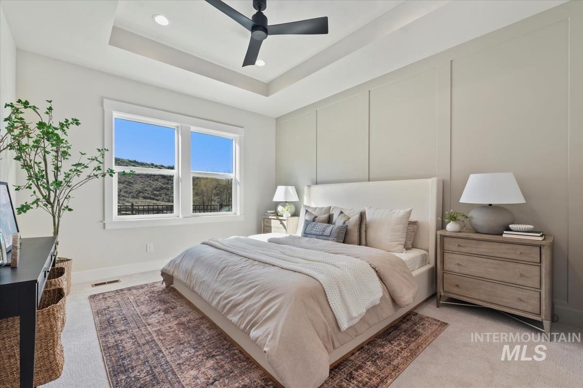 Bedroom with light carpet, a raised ceiling, a ceiling fan, a decorative wall, and recessed lighting
