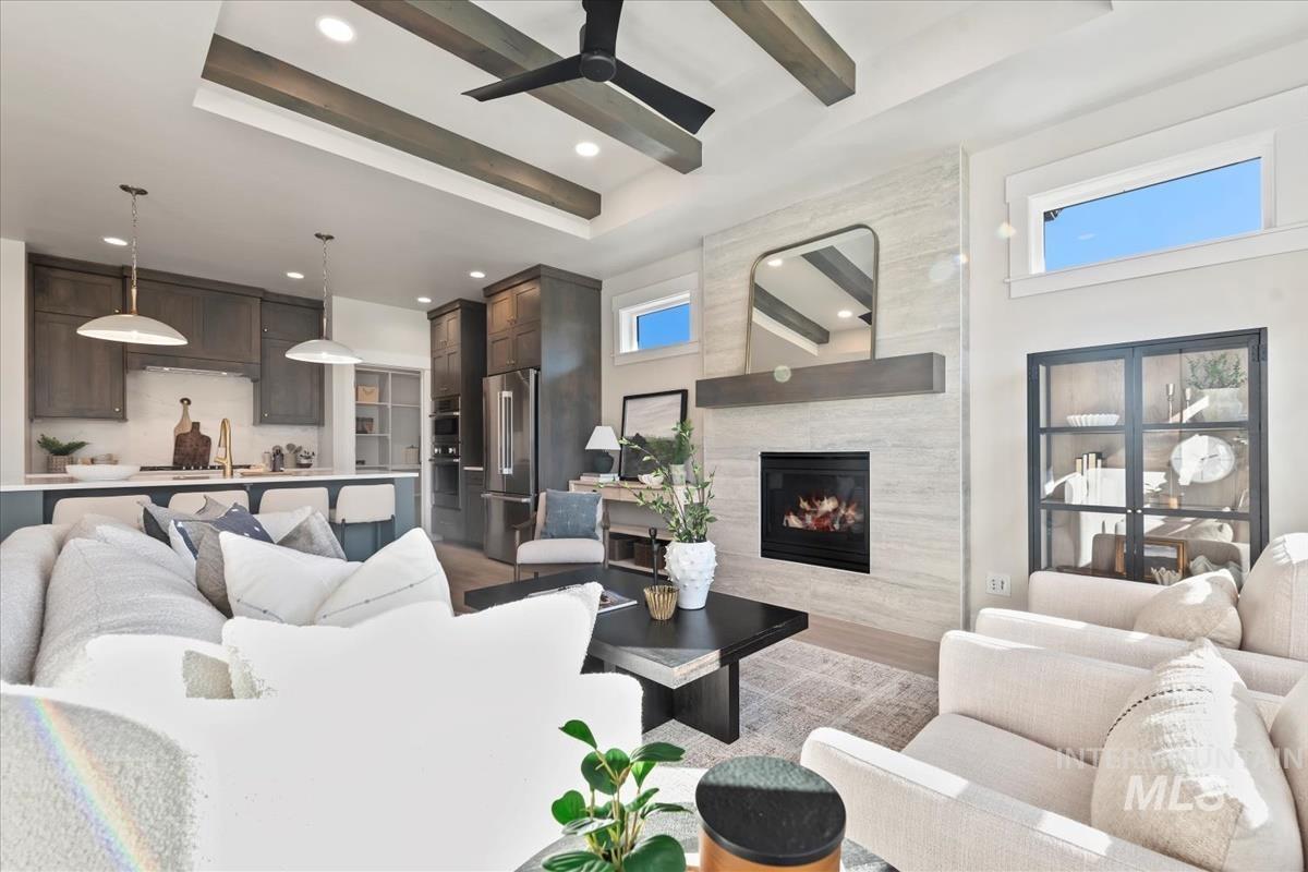 Living area with a tray ceiling, ceiling fan, a fireplace, recessed lighting, and beamed ceiling