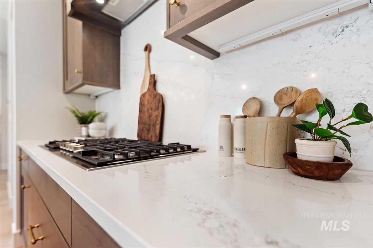 Kitchen view of stainless steel gas stovetop, exhaust hood, and light stone countertops
