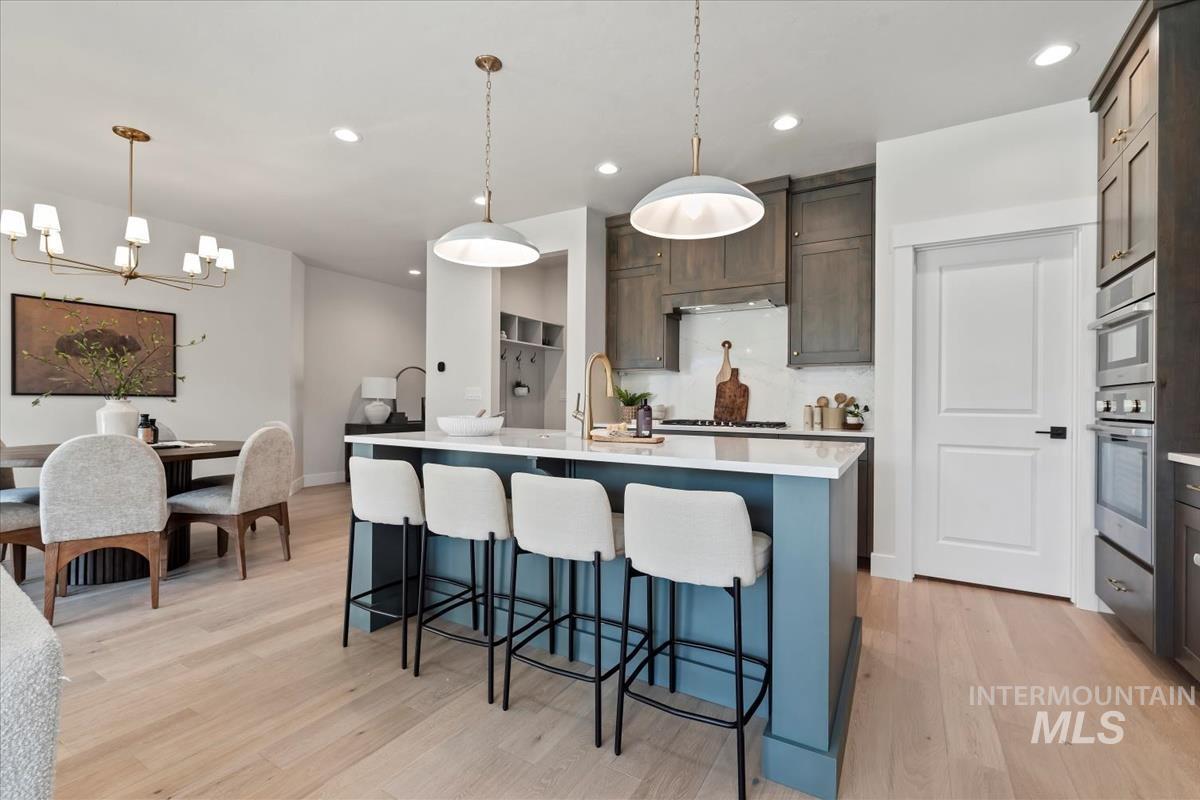Kitchen with a kitchen breakfast bar, decorative light fixtures, a kitchen island with sink, light wood-style flooring, and recessed lighting