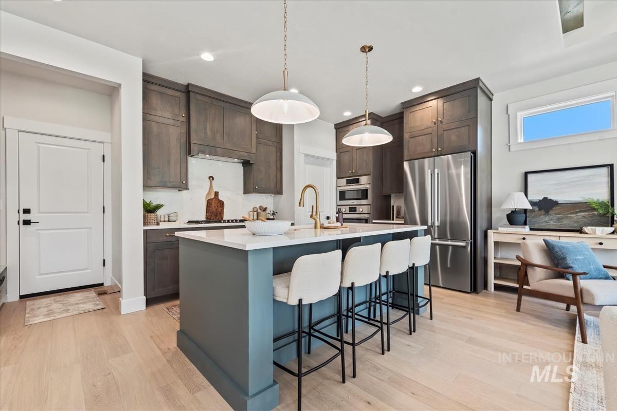 Kitchen featuring appliances with stainless steel finishes, an island with sink, a kitchen bar, hanging light fixtures, and light wood finished floors