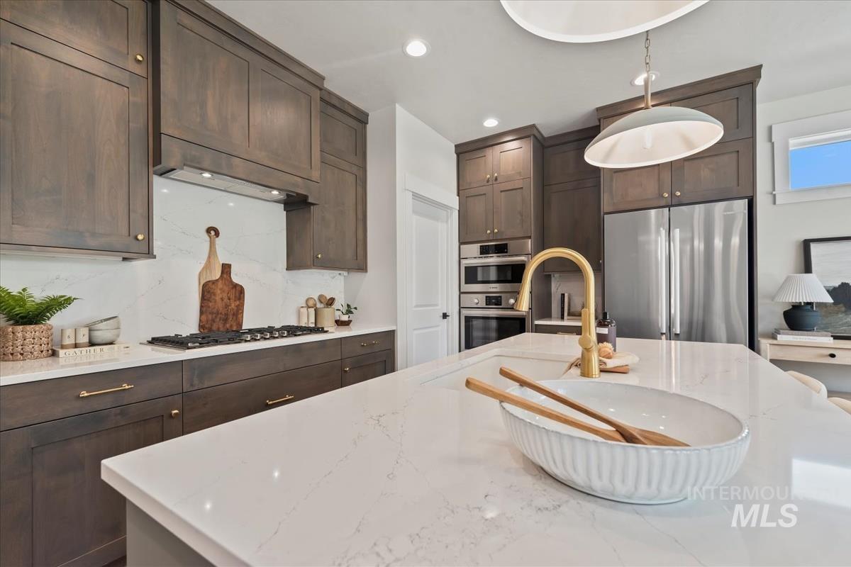 Kitchen with dark brown cabinetry, stainless steel appliances, light stone counters, pendant lighting, and decorative backsplash
