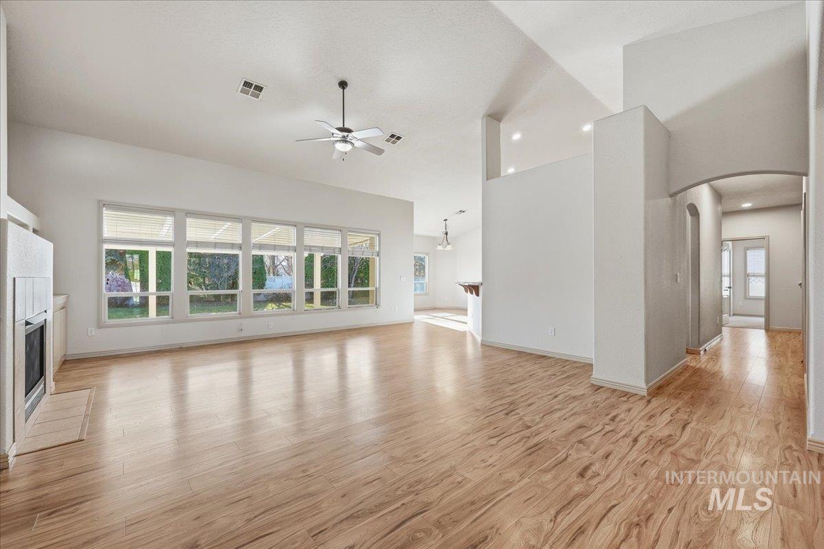 Unfurnished living room featuring a tile fireplace, light wood finished floors, arched walkways, ceiling fan, and plenty of natural light