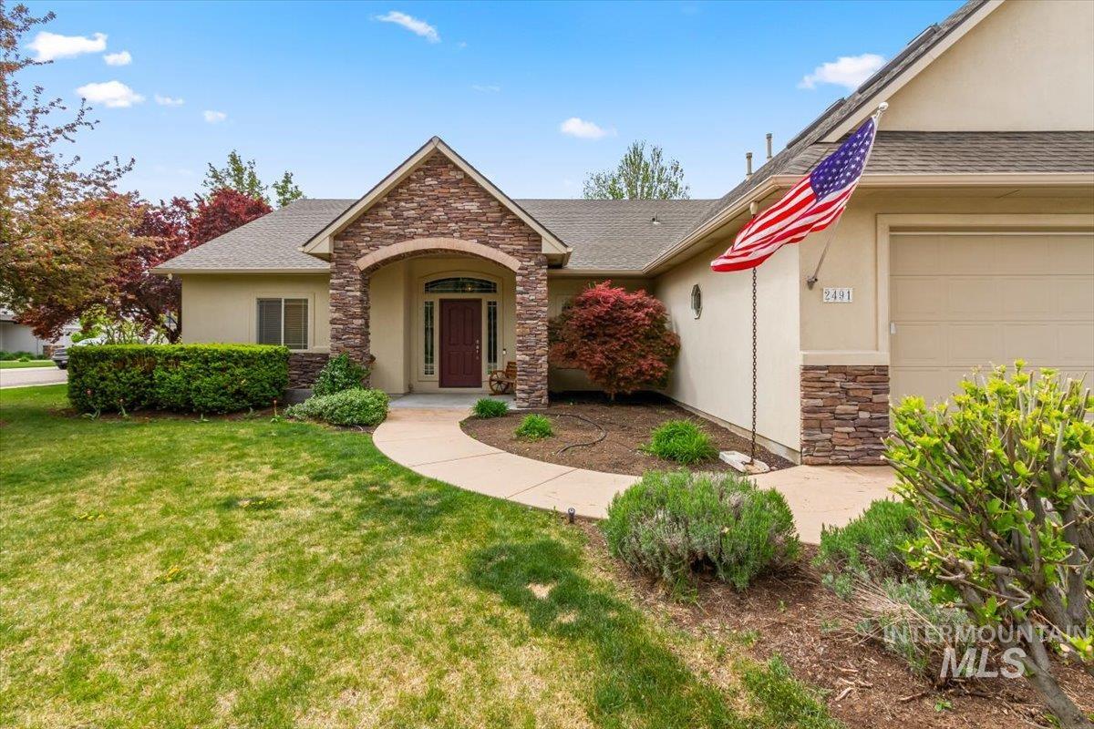 View of front of home featuring stone siding, stucco siding, a front yard, and a shingled roof