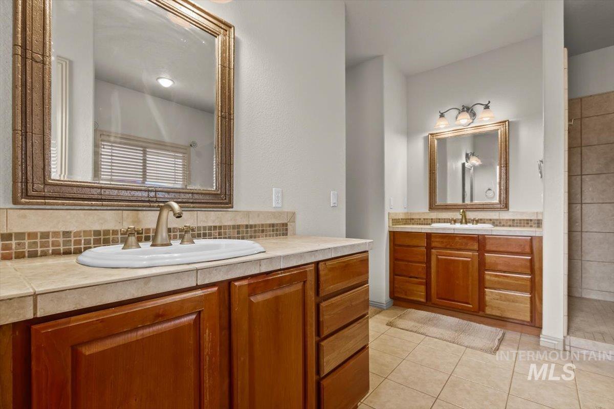 Full bathroom with two vanities, light tile patterned floors, a tile shower, and tasteful backsplash
