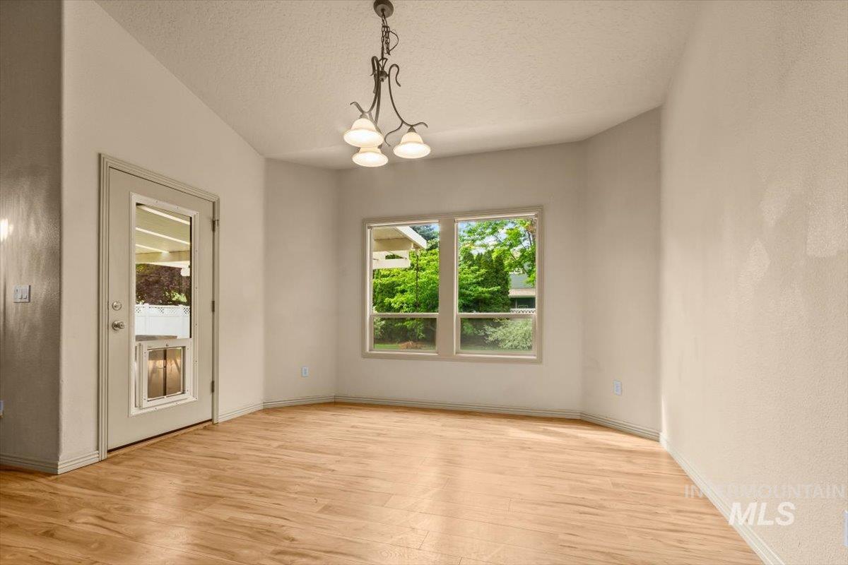 Empty room with a chandelier, light wood-type flooring, and a textured ceiling