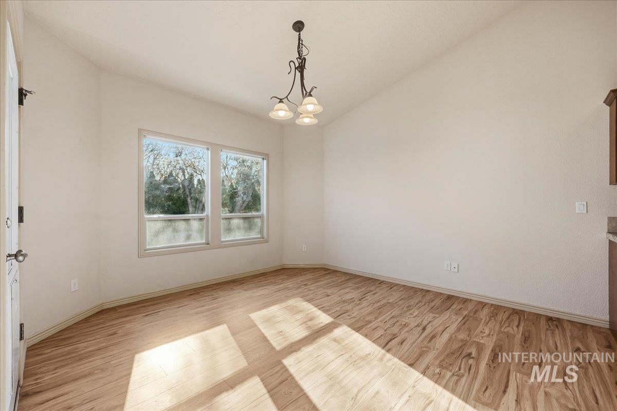 Unfurnished room featuring light wood finished floors, a chandelier, and lofted ceiling