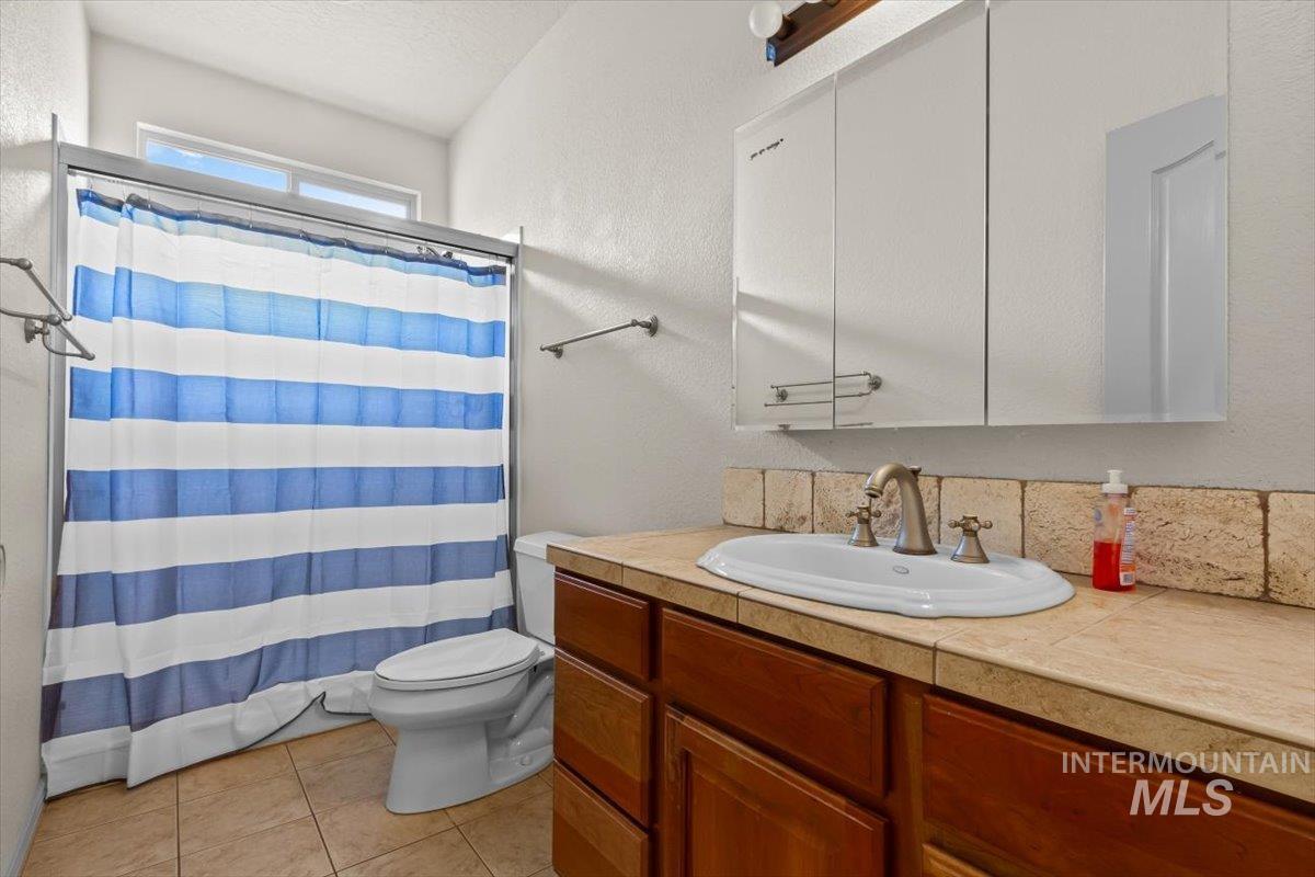 Full bath with a shower with curtain, vanity, a textured wall, and light tile patterned flooring