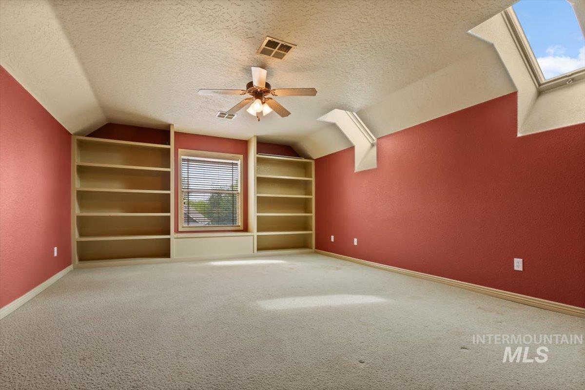 Additional living space featuring built in shelves, a textured ceiling, a ceiling fan, carpet, and vaulted ceiling