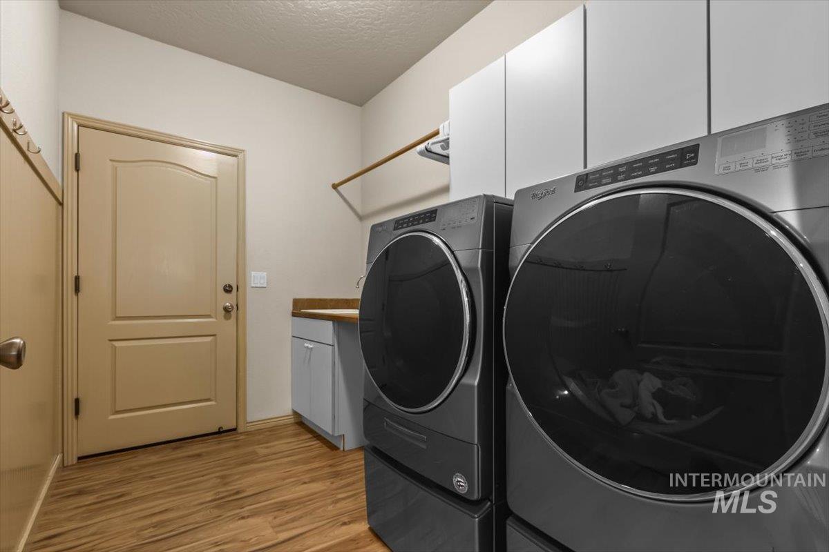 Laundry area with a textured ceiling, light wood-style floors, cabinet space, and washer and clothes dryer