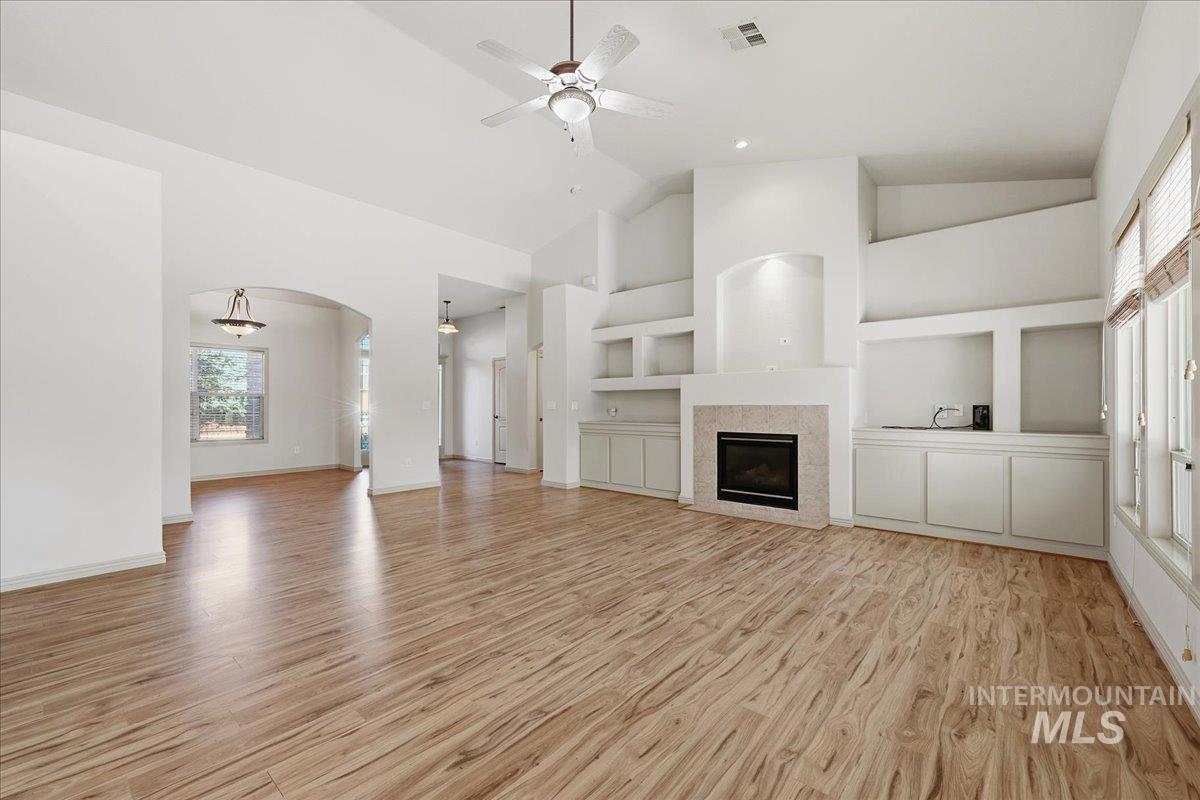 Unfurnished living room with built in features, arched walkways, light wood-style flooring, high vaulted ceiling, and a ceiling fan