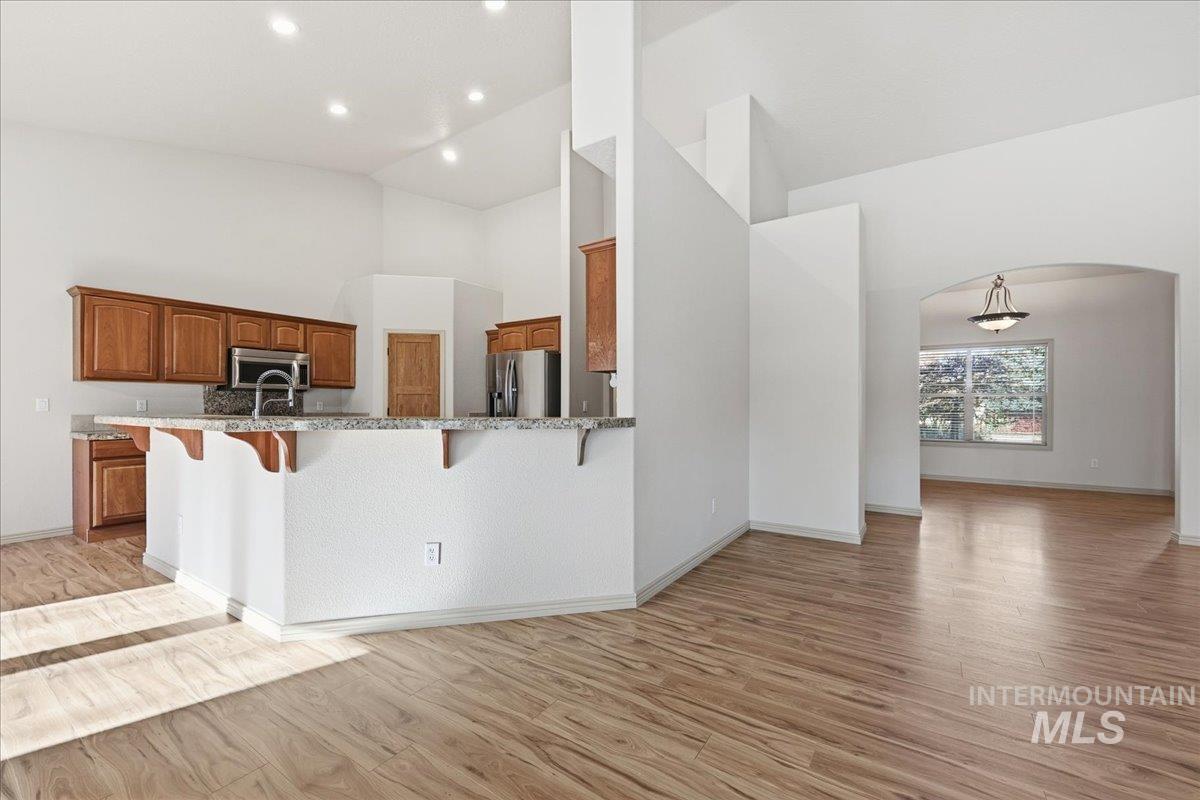 Kitchen featuring a kitchen bar, arched walkways, brown cabinets, high vaulted ceiling, and light wood finished floors