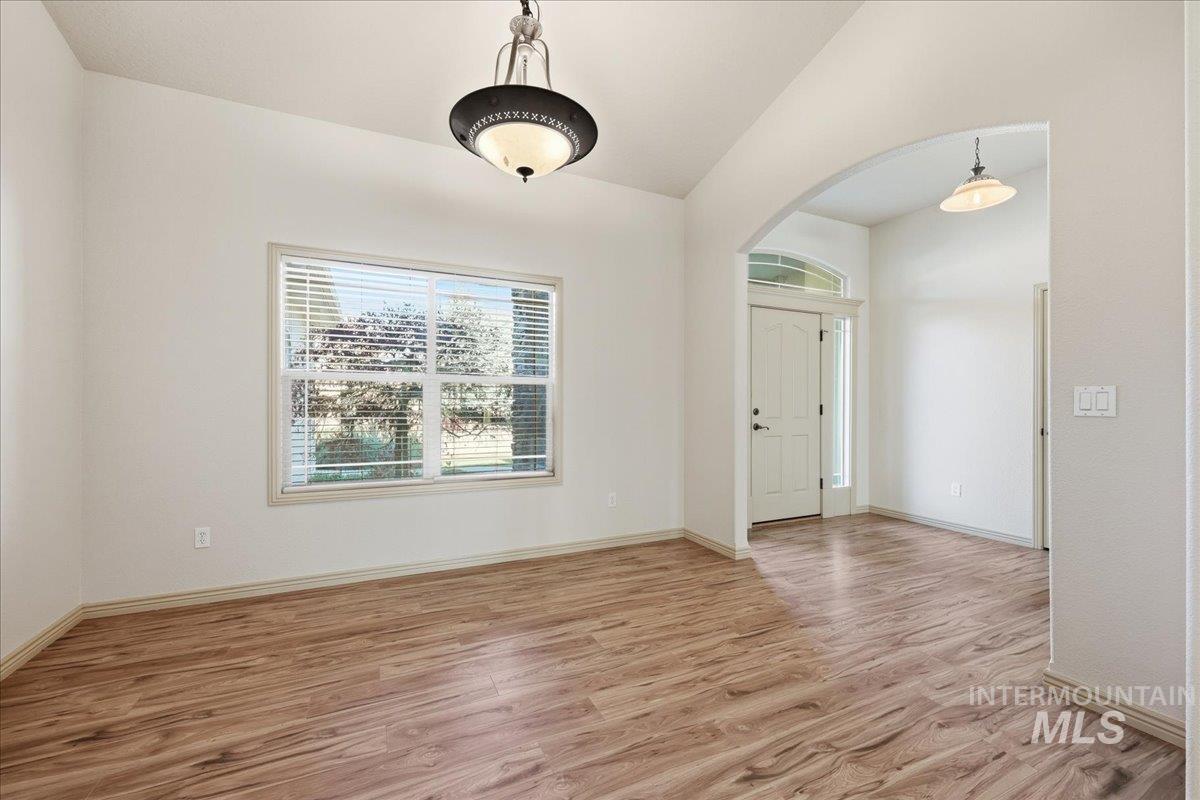 Empty room featuring light wood finished floors, arched walkways, and vaulted ceiling