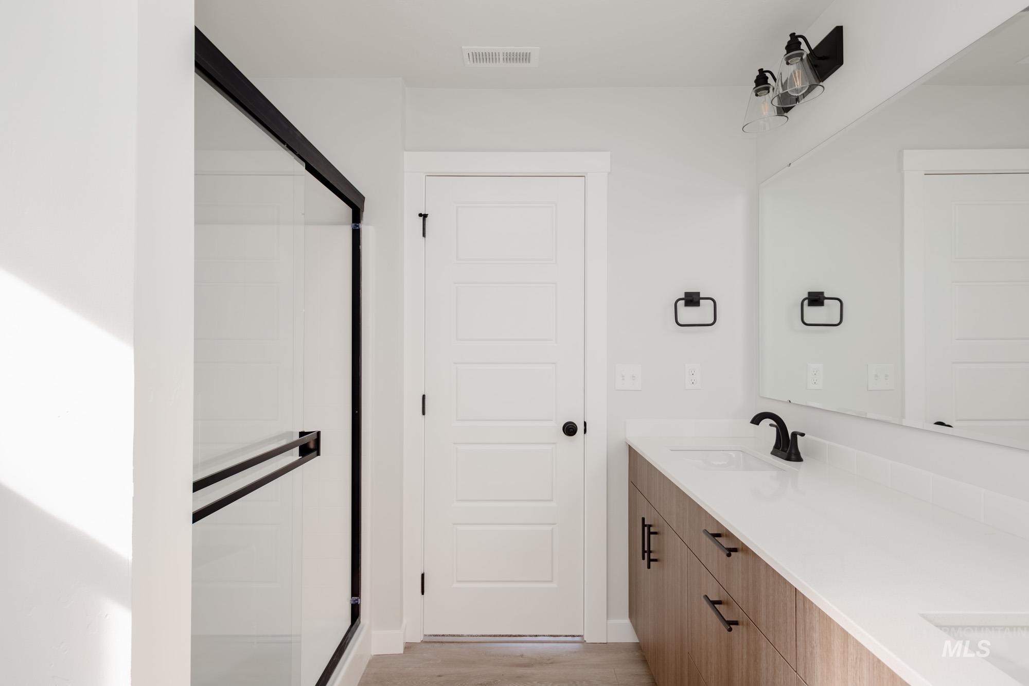 Full bathroom with double vanity, a shower stall, and light wood-style floors