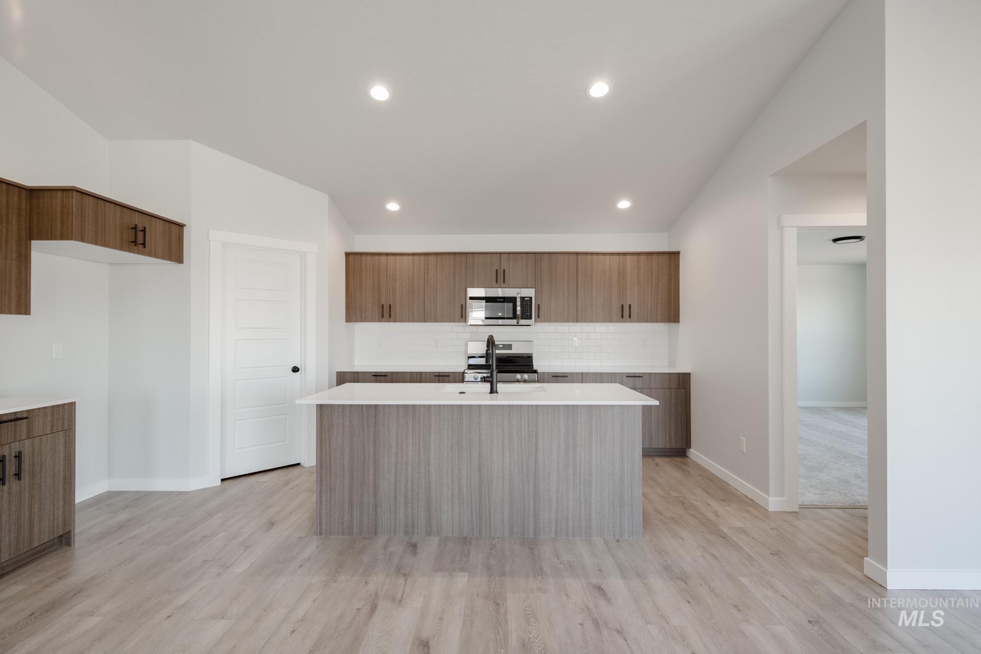 Kitchen with modern cabinets, an island with sink, appliances with stainless steel finishes, light stone countertops, and recessed lighting