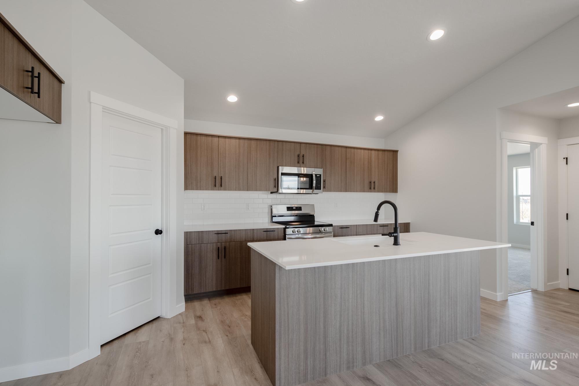 Kitchen with modern cabinets, stainless steel appliances, a center island with sink, light wood-style flooring, and light stone counters