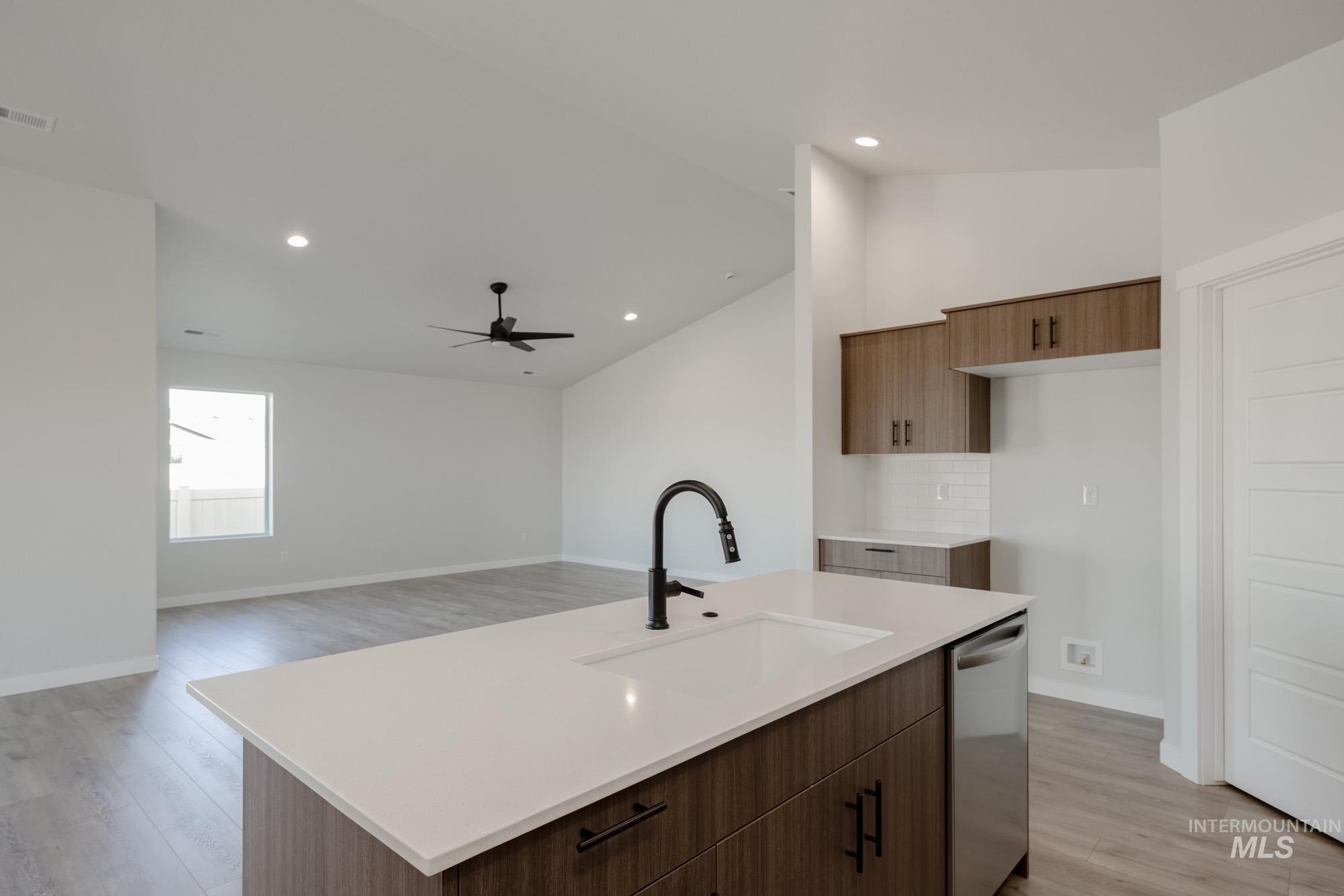 Kitchen with vaulted ceiling, decorative backsplash, light wood-type flooring, an island with sink, and modern cabinets