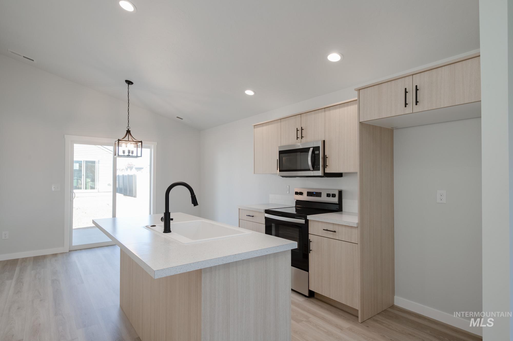 Kitchen with light brown cabinetry, appliances with stainless steel finishes, light countertops, recessed lighting, and lofted ceiling