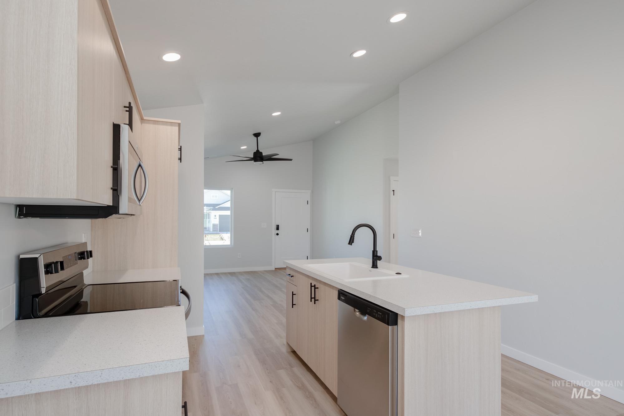 Kitchen with light brown cabinets, light countertops, appliances with stainless steel finishes, an island with sink, and vaulted ceiling