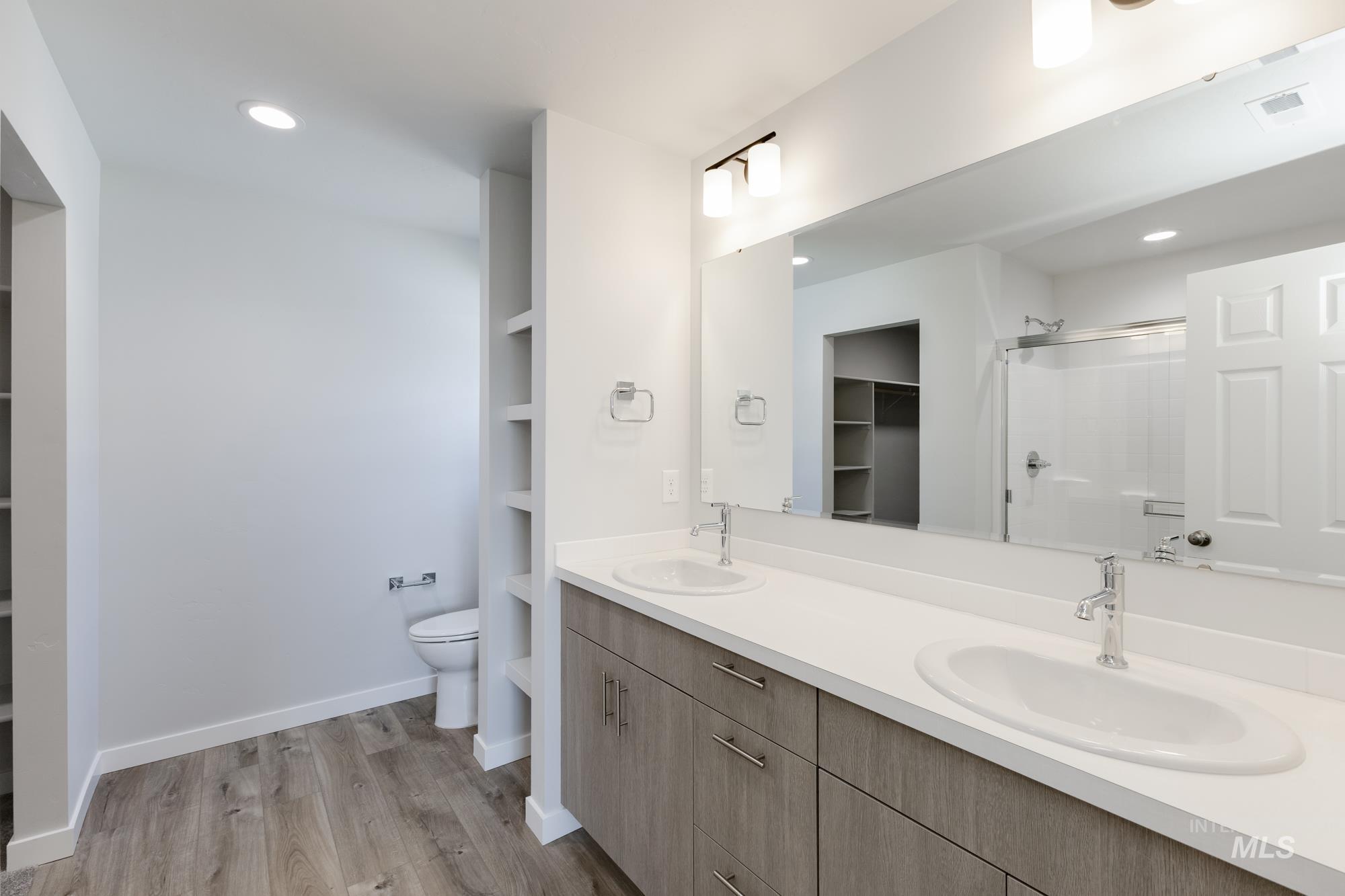 Bathroom with a spacious closet, double vanity, a shower stall, light wood-type flooring, and built in shelves