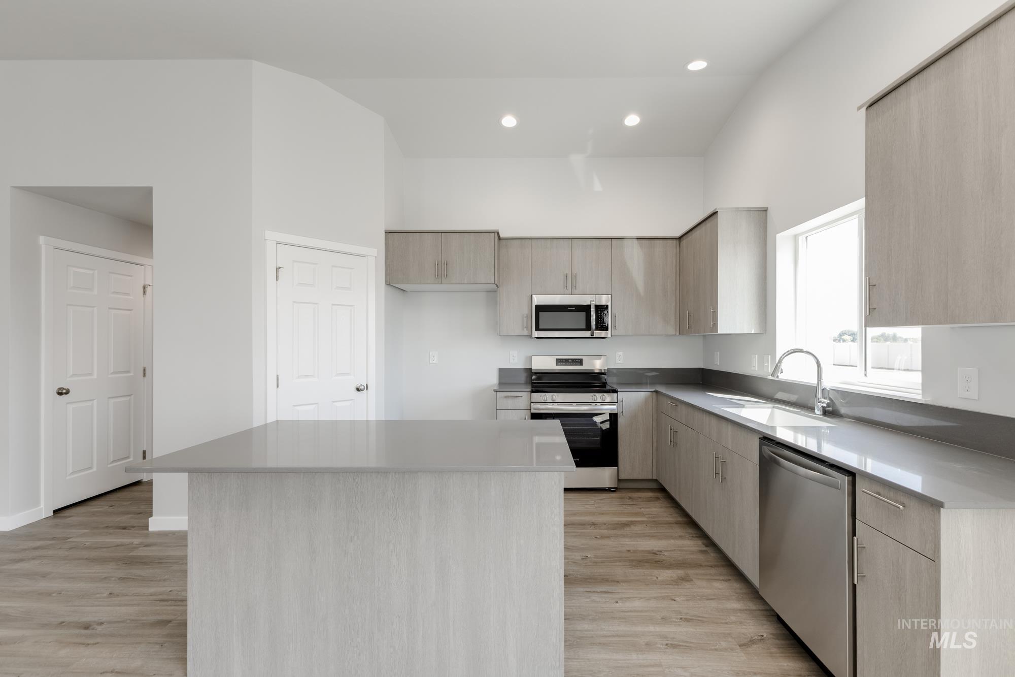 Kitchen with stainless steel appliances, modern cabinets, light brown cabinets, a kitchen island, and light wood-style floors