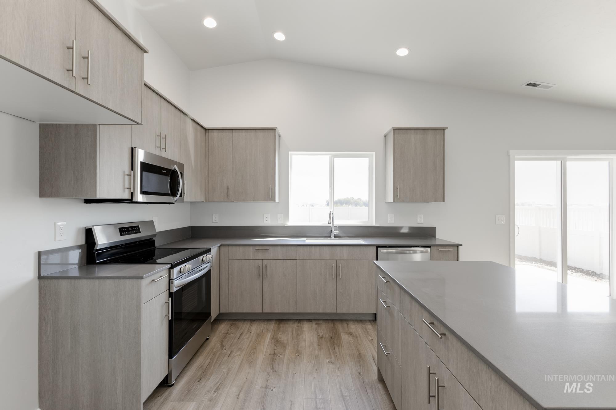 Kitchen with light brown cabinetry, stainless steel appliances, modern cabinets, lofted ceiling, and light wood-style floors