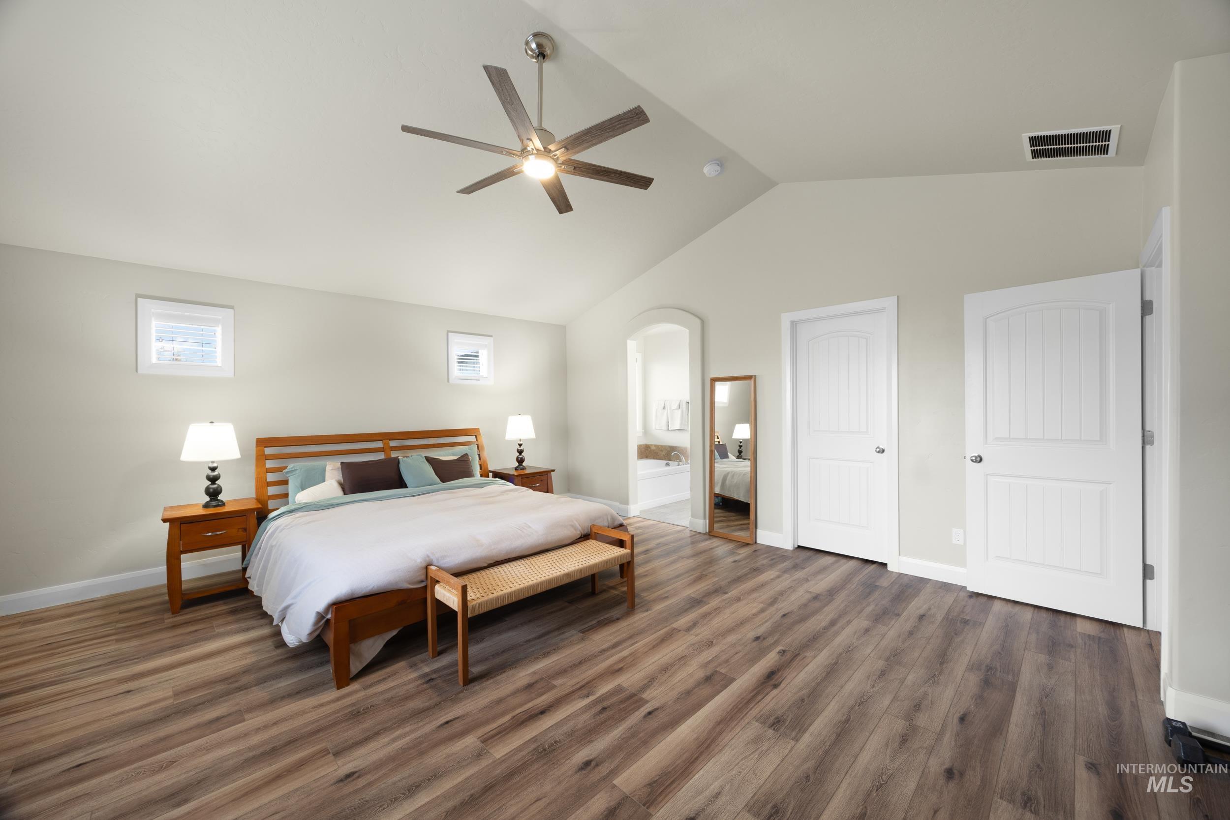 Bedroom with lofted ceiling, wood finished floors, a ceiling fan, arched walkways, and ensuite bath