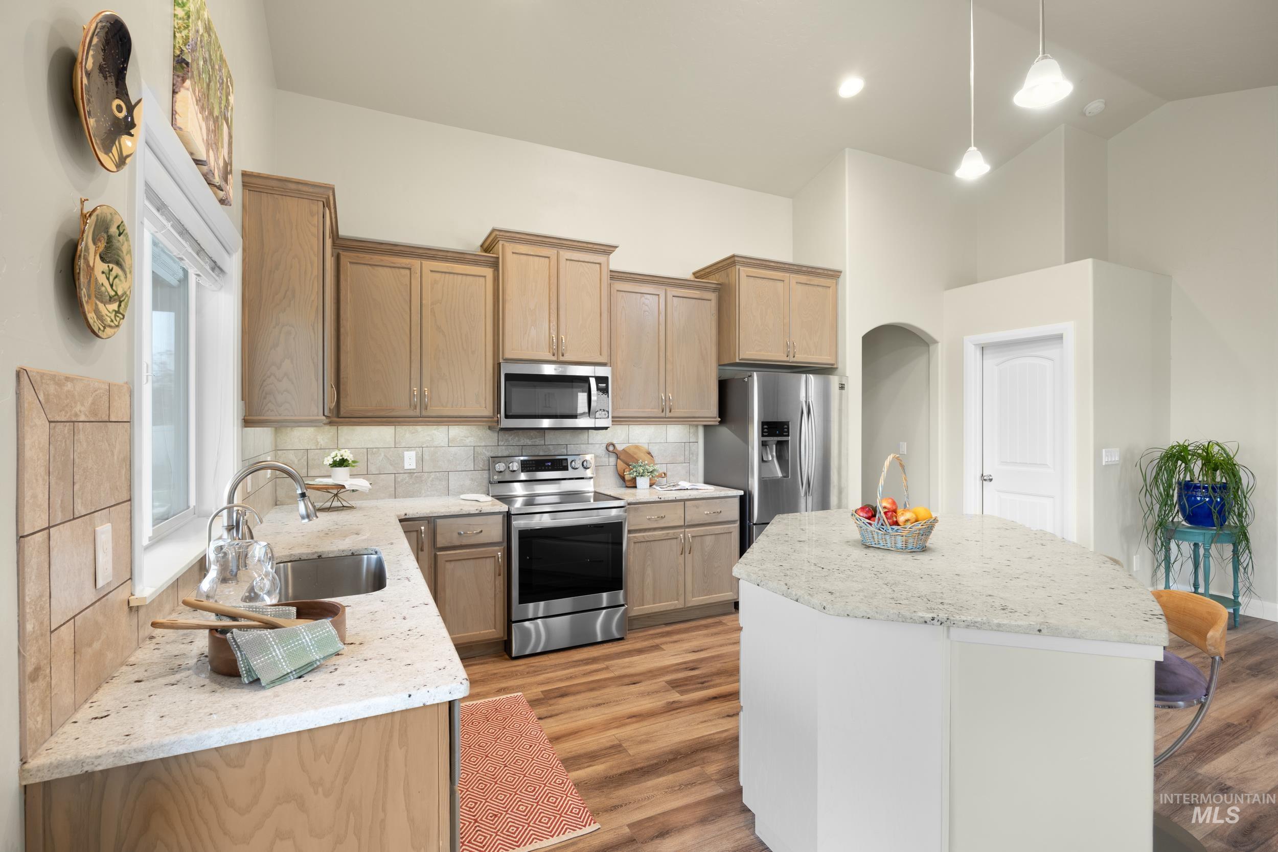 Kitchen featuring appliances with stainless steel finishes, light stone counters, hanging light fixtures, a center island, and high vaulted ceiling