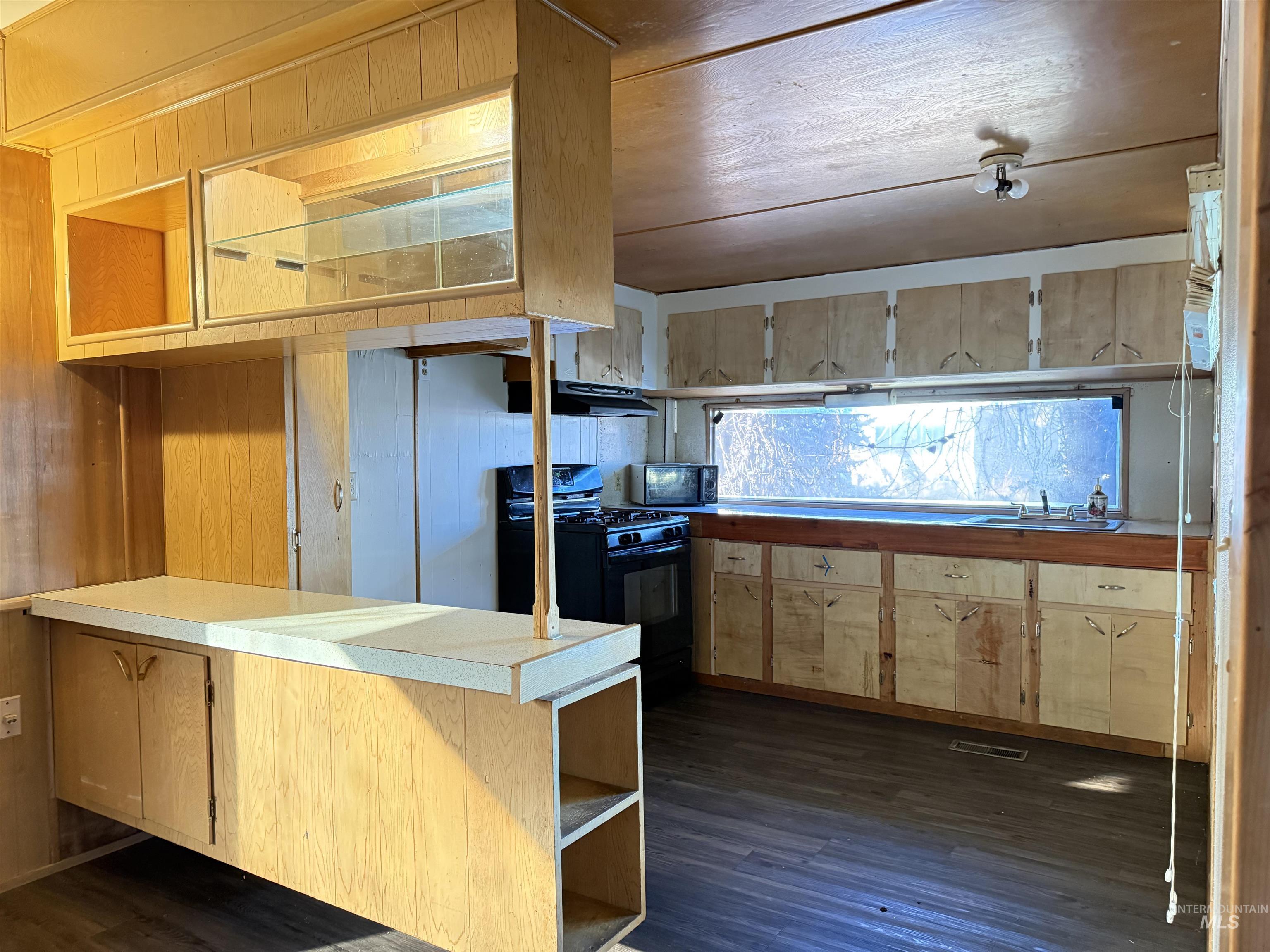 Kitchen with open shelves, black appliances, dark wood-type flooring, light countertops, and wooden walls