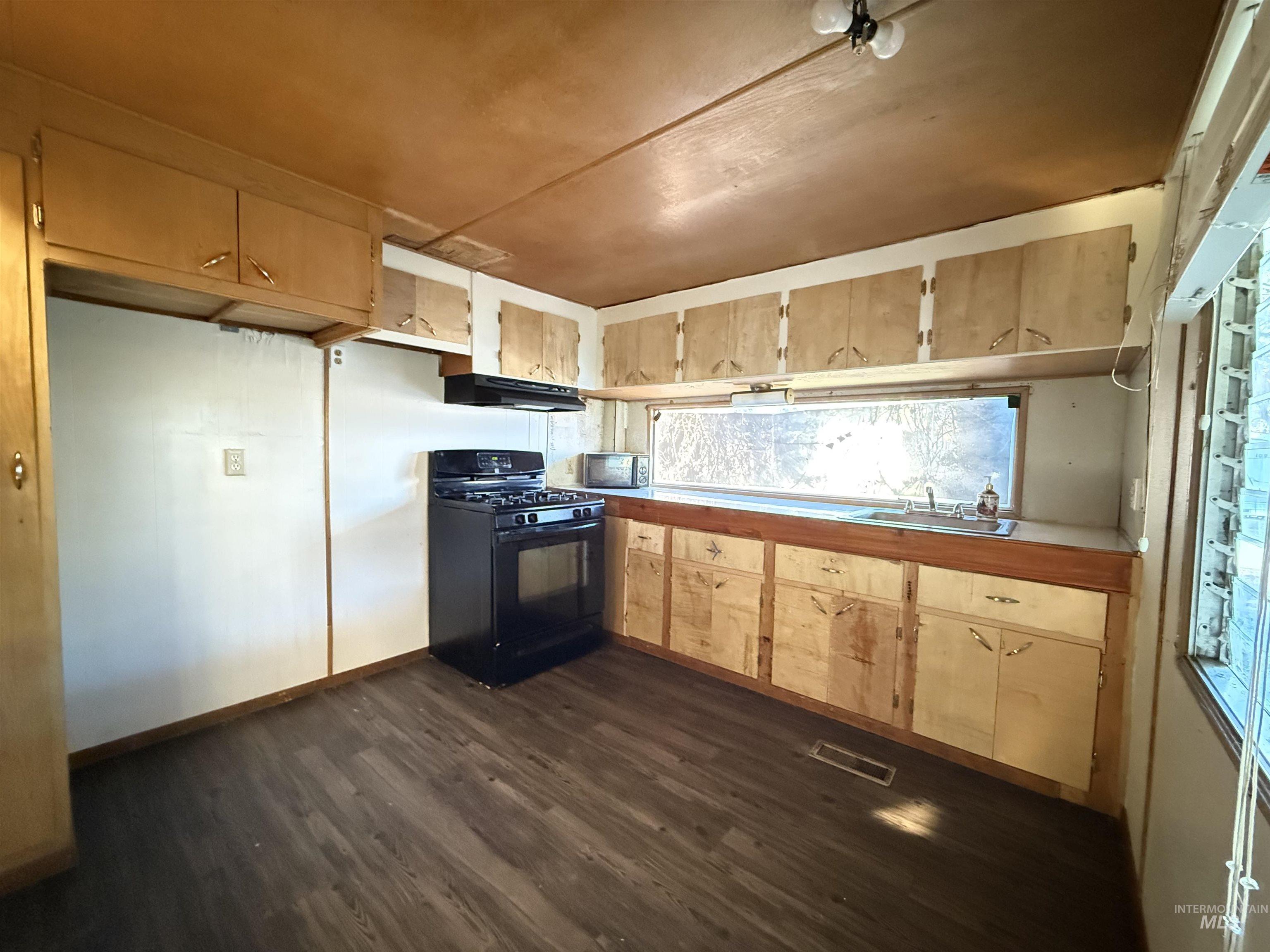 Kitchen with gas stove, dark wood finished floors, light brown cabinets, and light countertops
